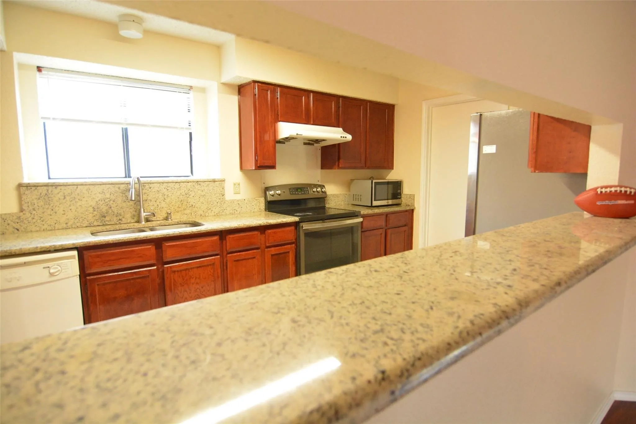 Kitchen featuring wood cabinetry, light-toned countertops, a stainless steel sink with a gooseneck faucet, and a built-in electric range with an overhead vent