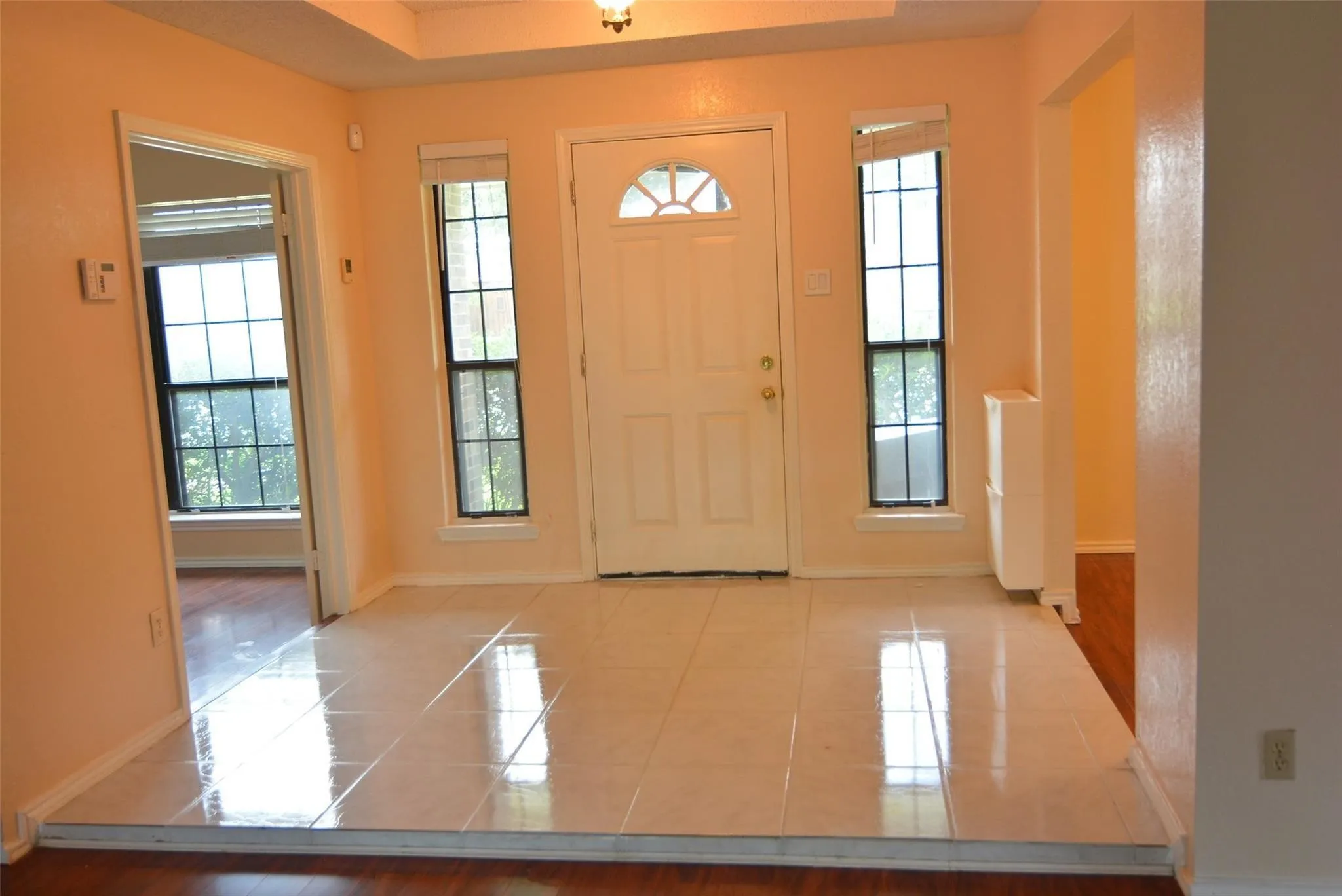Entryway featuring a tray ceiling, tiled flooring, sidelight windows, and a panel door with an arched lite
