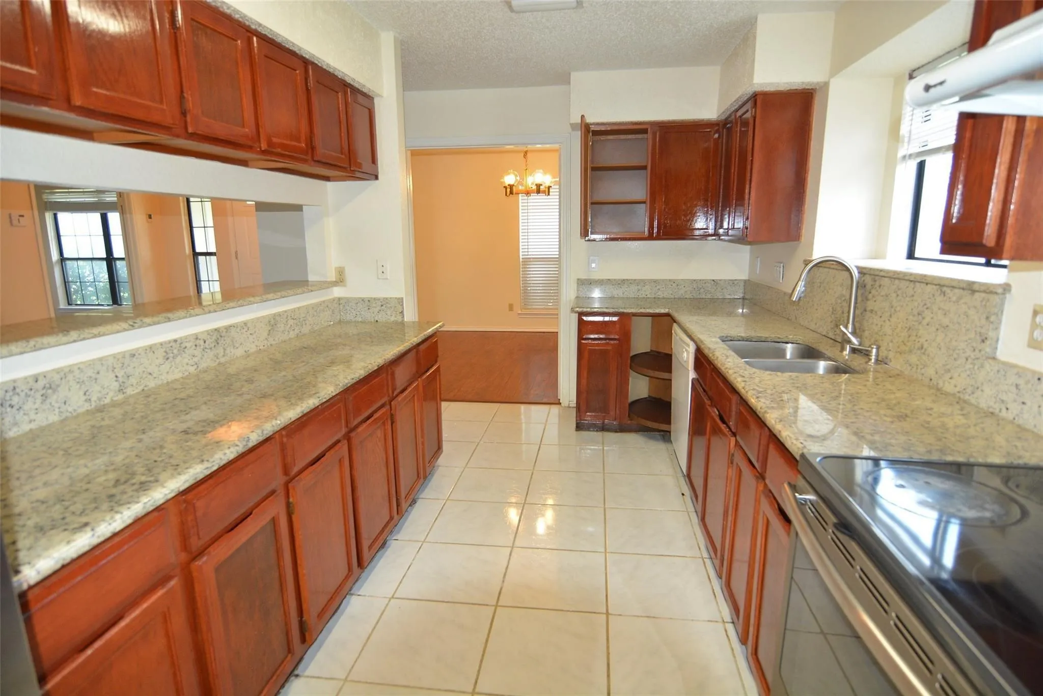 Kitchen featuring wood cabinetry, light-toned stone countertops, a double basin stainless steel sink, and tile flooring