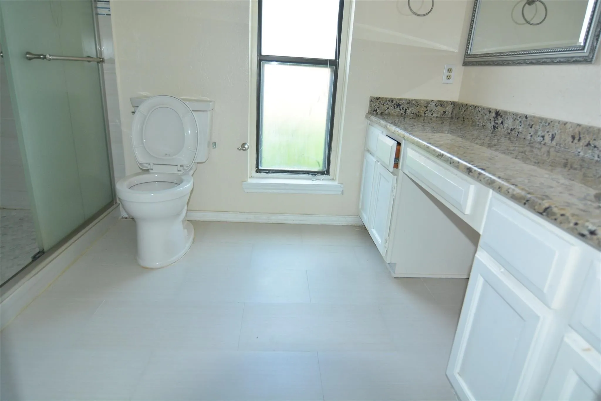 White cabinetry with a granite-look countertop, integrated window, and a glass-enclosed shower