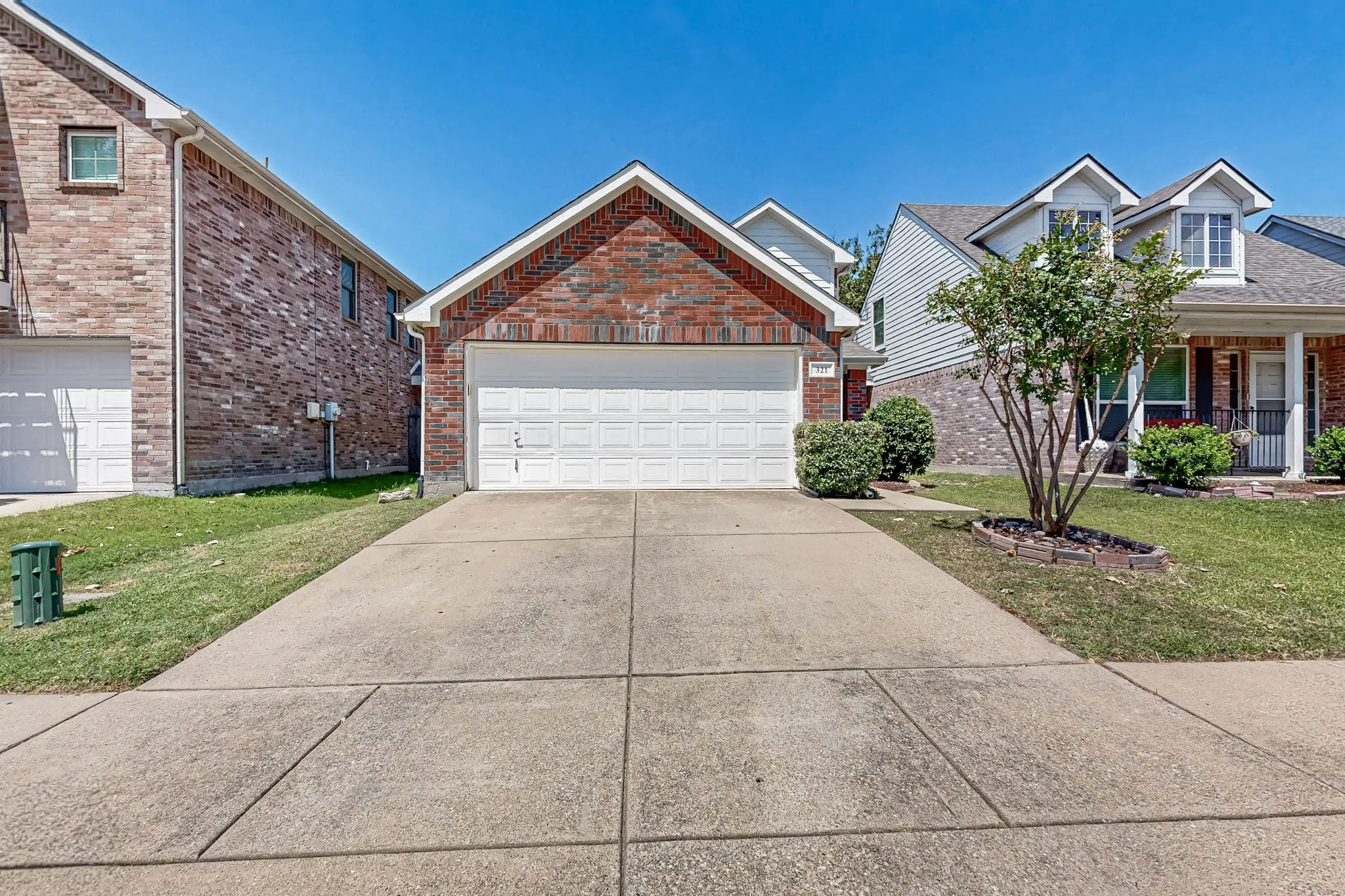 Brick exterior with an attached garage, concrete driveway, and manicured landscaping