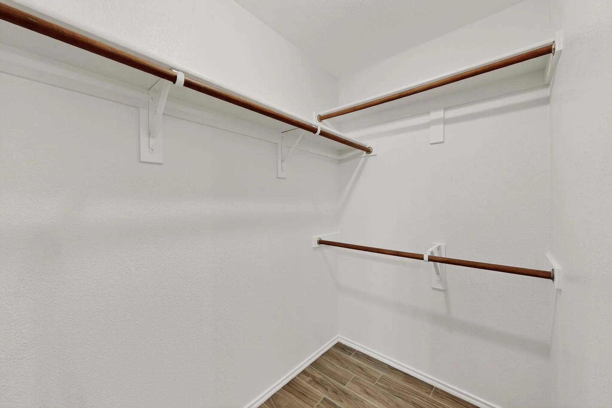 Expansive closet featuring multiple hanging rods, integrated shelving, and wood-finish flooring