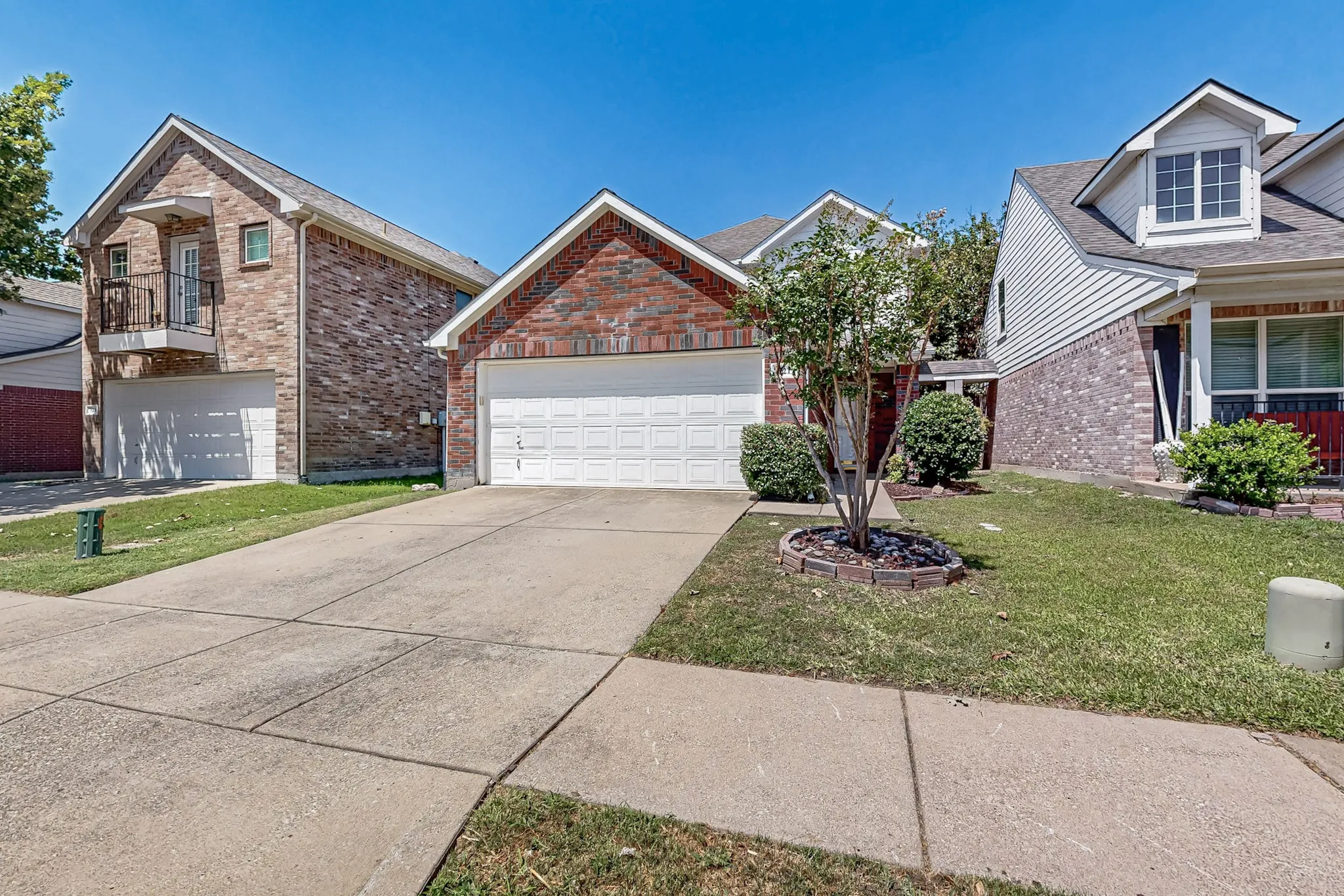 Brick facade with an attached two-car garage, concrete driveway, and mature landscaping