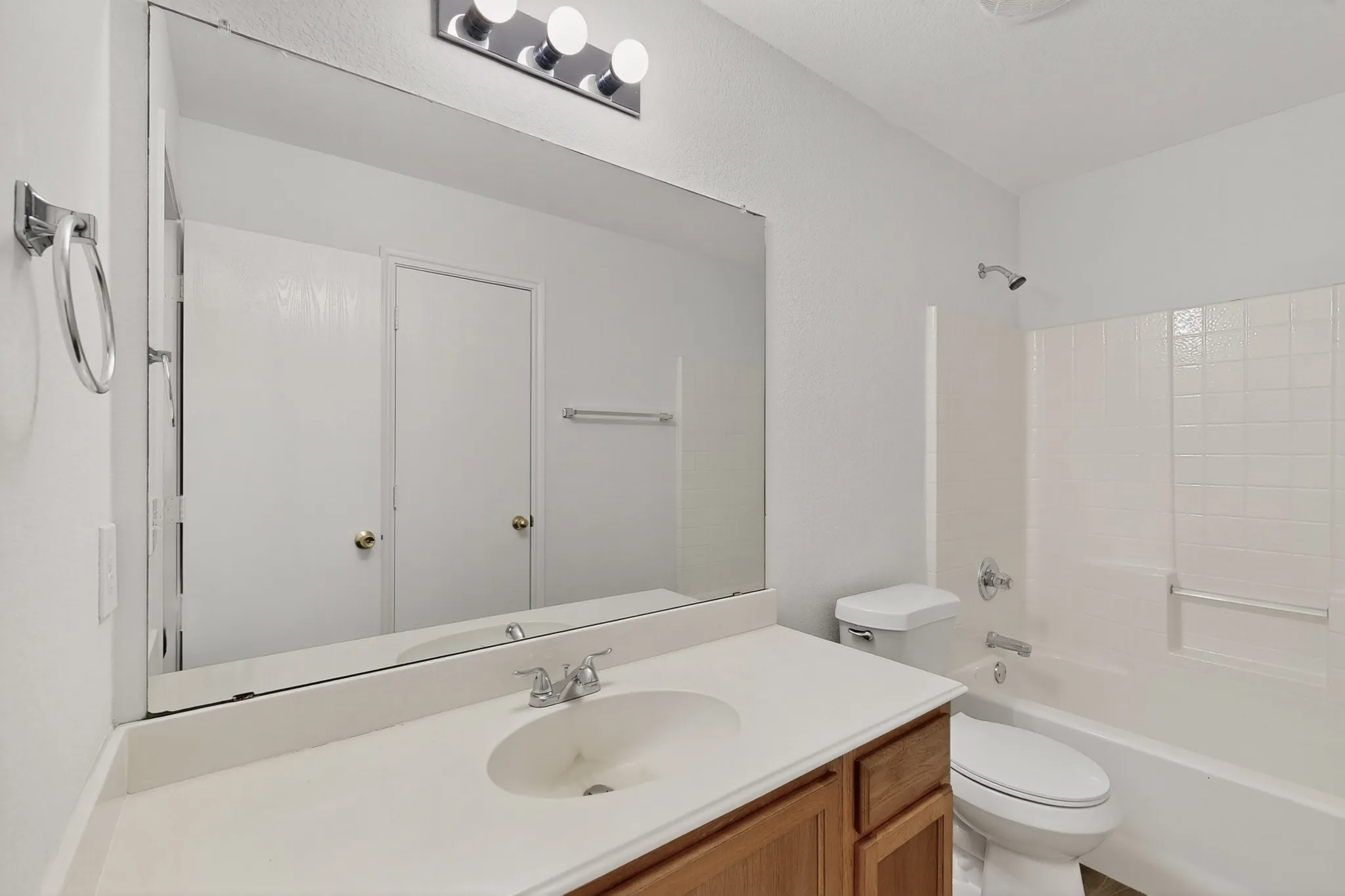 Spa-inspired bathroom featuring a large framed mirror above a wood-finish vanity with undermount sink and white quartz countertop, chrome faucet and hardware, recessed lighting, and an enclosed shower-tub combination with tile surround and glass enclosure