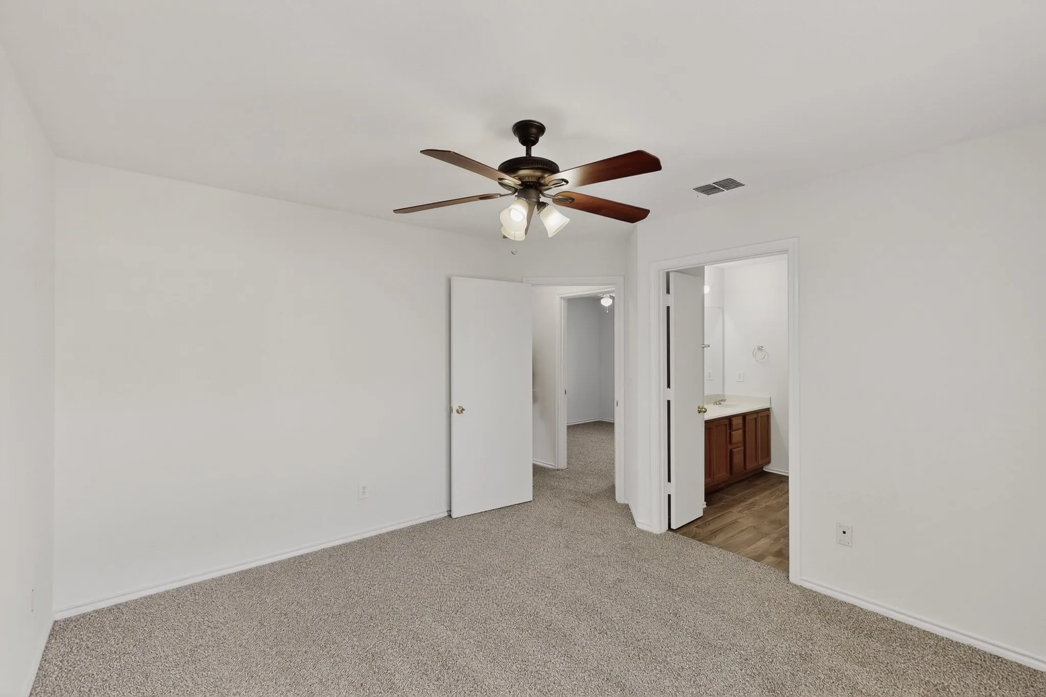 Neutral-toned carpeting, ceiling fan with light fixture, and white interior doors