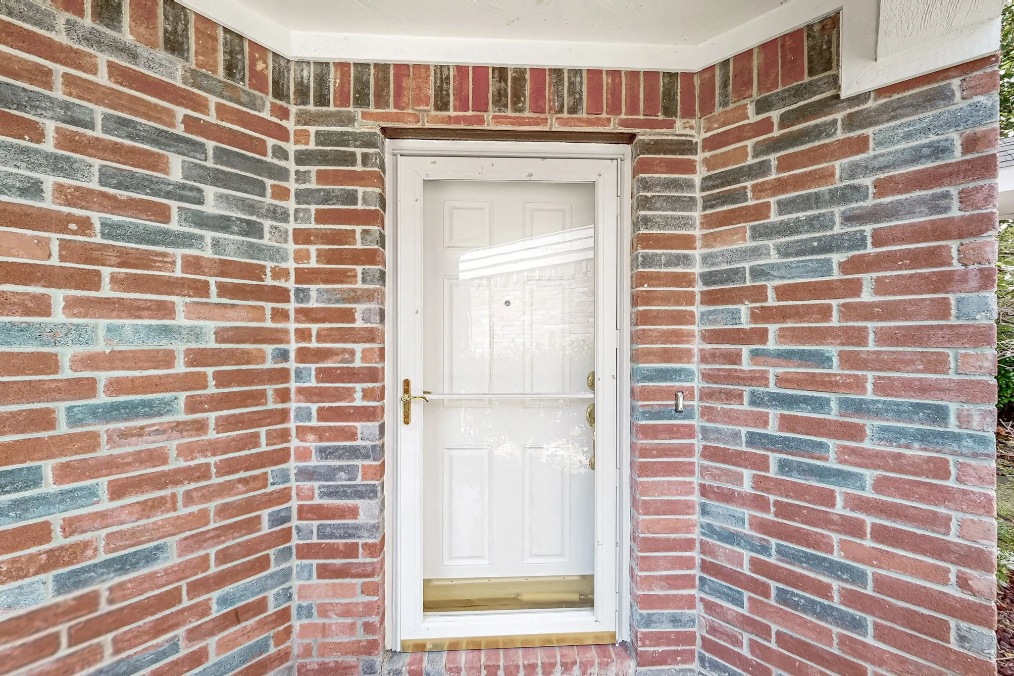 Entryway featuring a white paneled door with a screen door and a two-tone brick facade