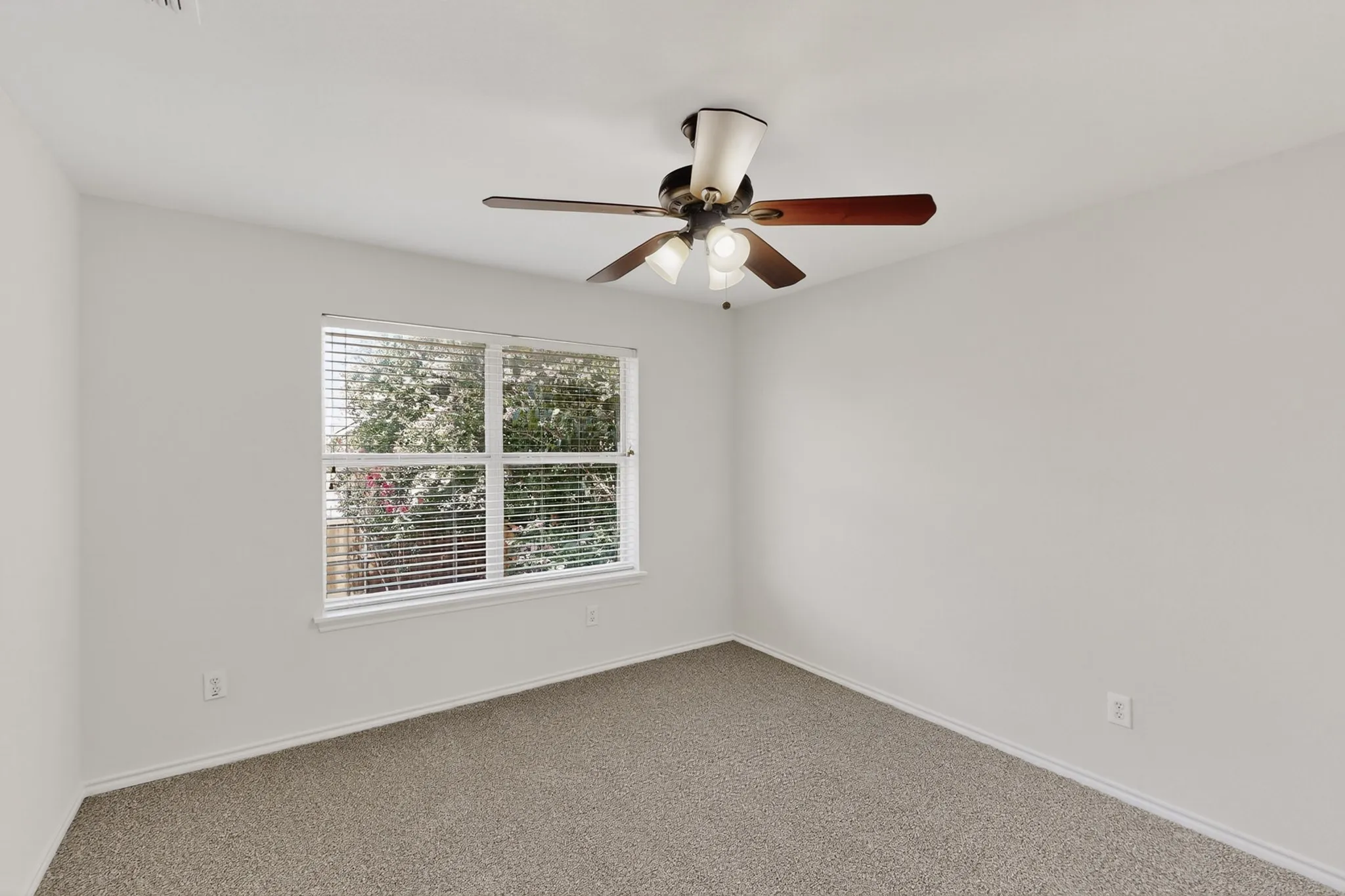 Neutral wall paint, textured carpeting, a window with horizontal blinds, and a ceiling fan with integrated lighting