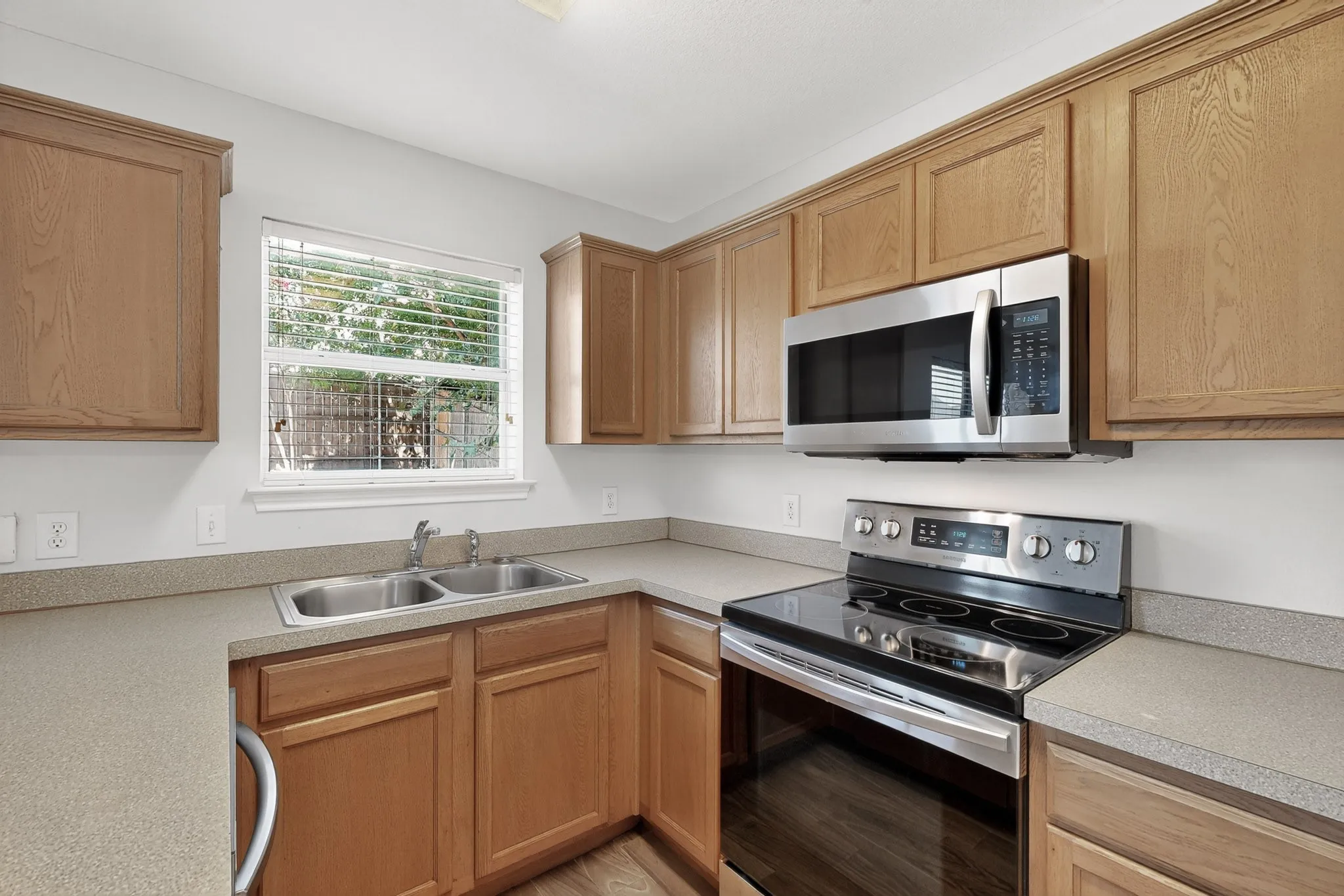 Wood-finish cabinetry, stainless steel microwave, stainless steel electric range, double basin stainless steel sink, and light-colored countertops