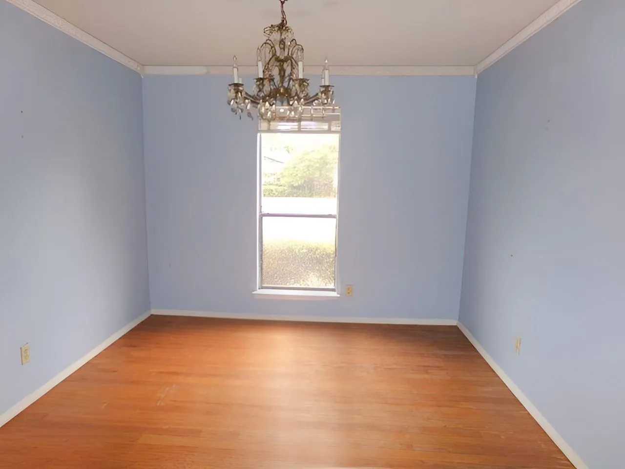Wood-finish flooring with crown molding and a central chandelier