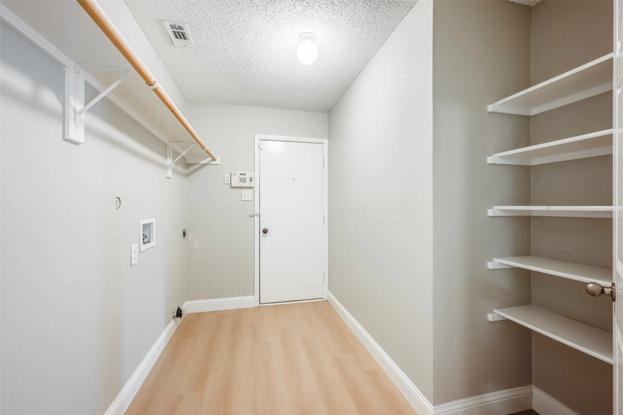 Laundry area with wood-finish flooring, built-in shelving, and a hanging rod