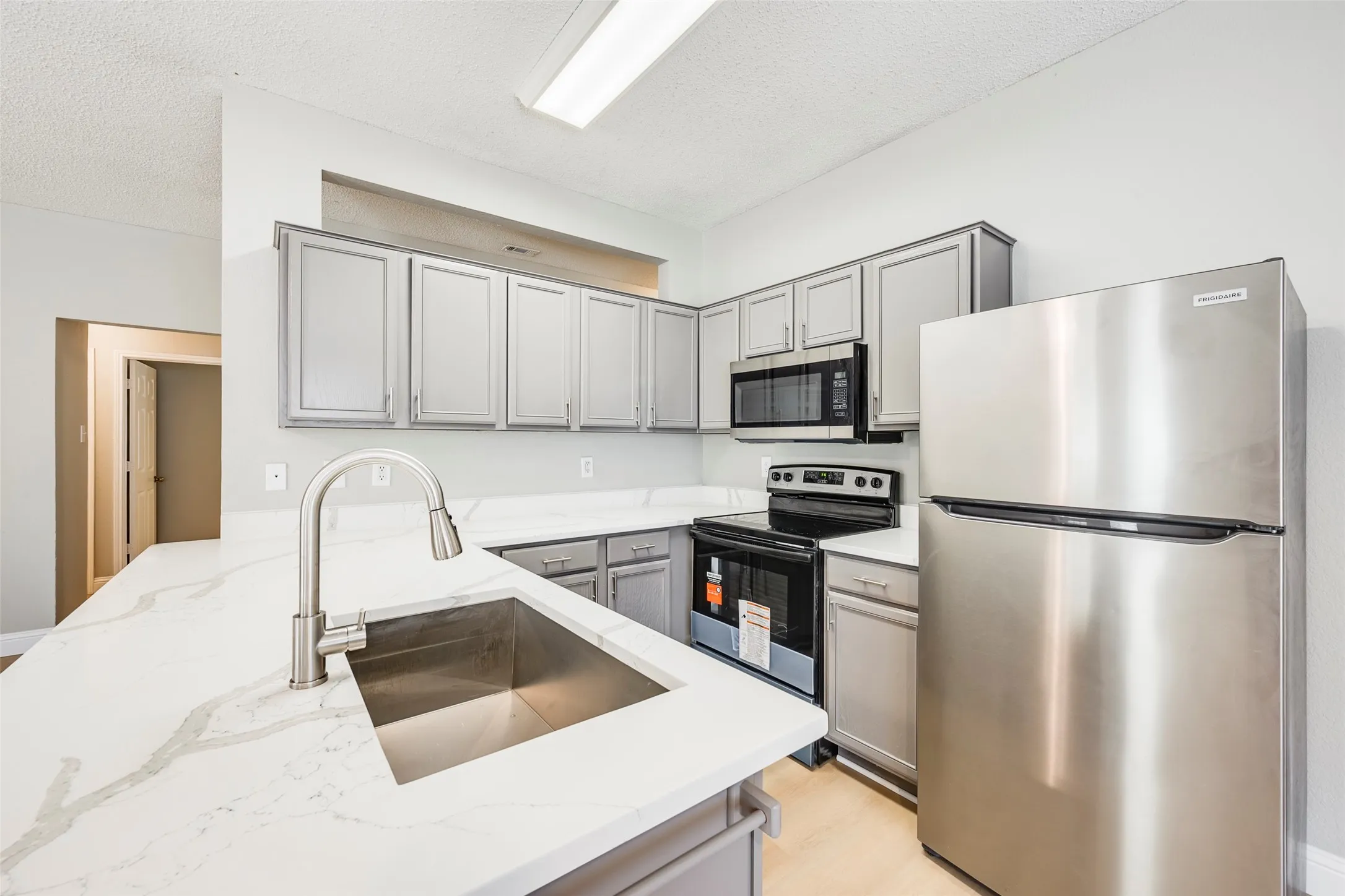 Kitchen featuring gray cabinetry, stainless steel appliances, a built-in microwave, and a single basin sink with a brushed nickel faucet