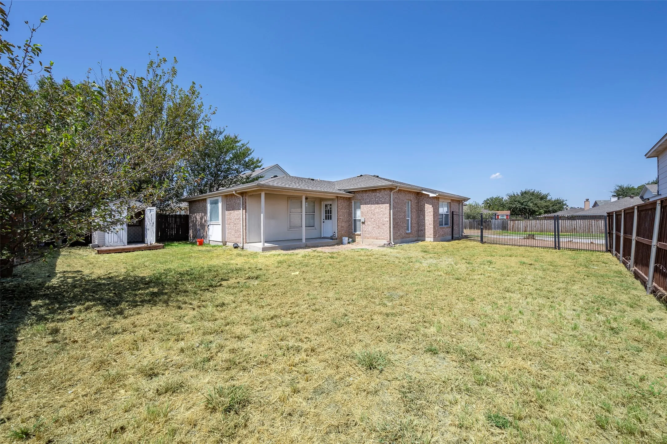 Expansive backyard featuring a covered patio, a detached storage shed, privacy fencing, and mature trees