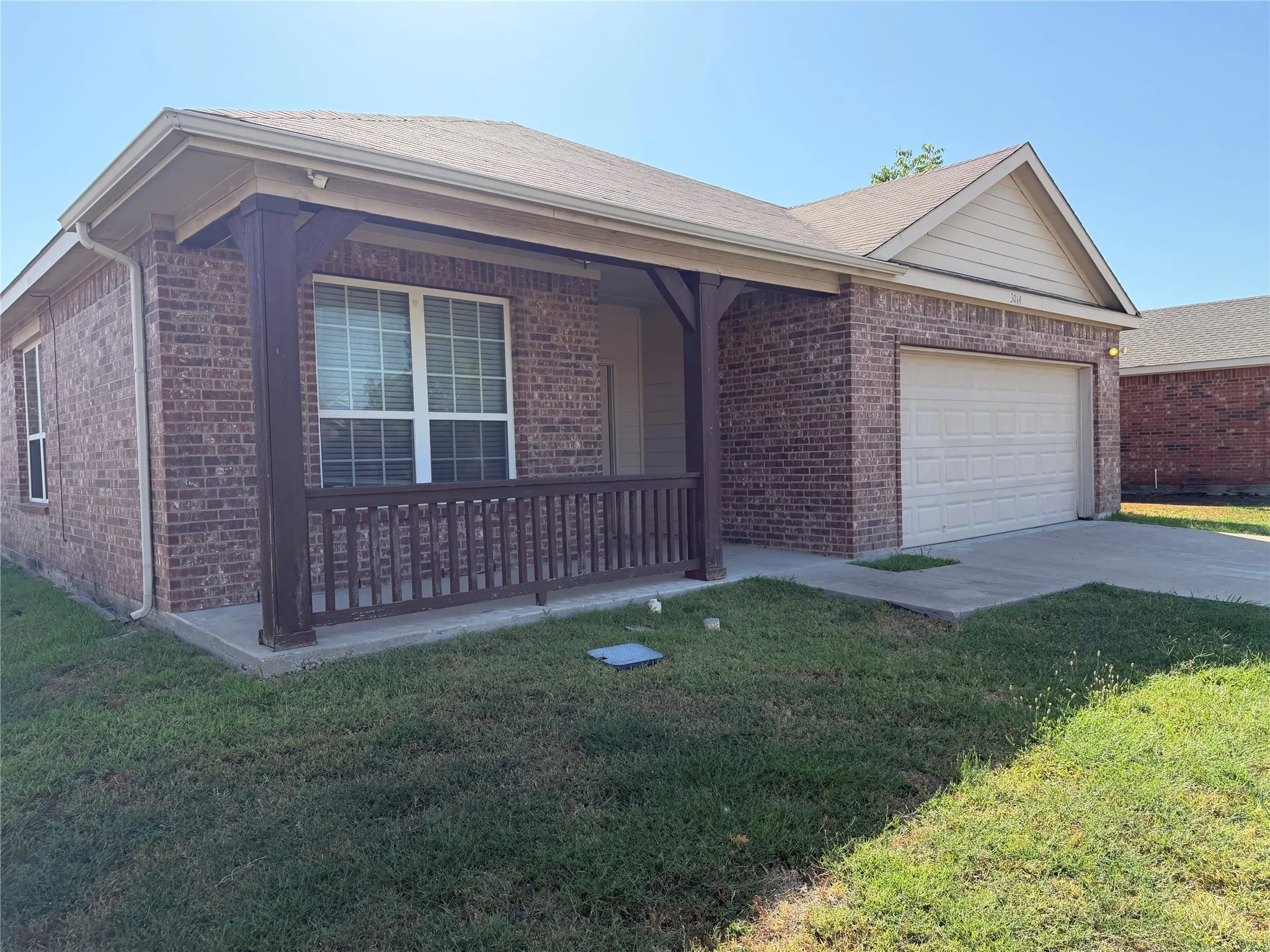 Brick exterior with covered front porch, white window blinds, and an attached garage