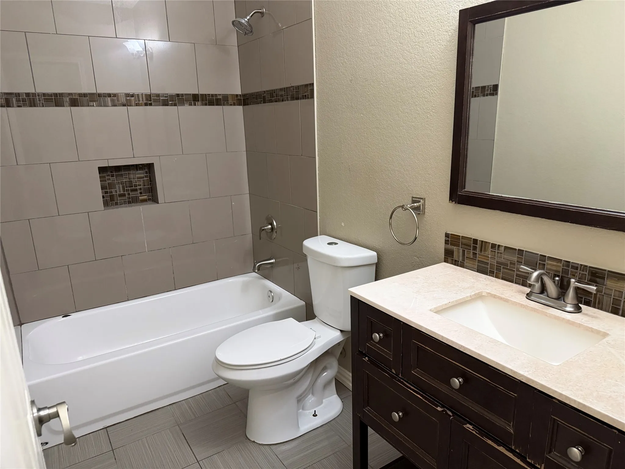Bathroom featuring a white tub, tiled shower surround with mosaic accent, and a built-in shower niche