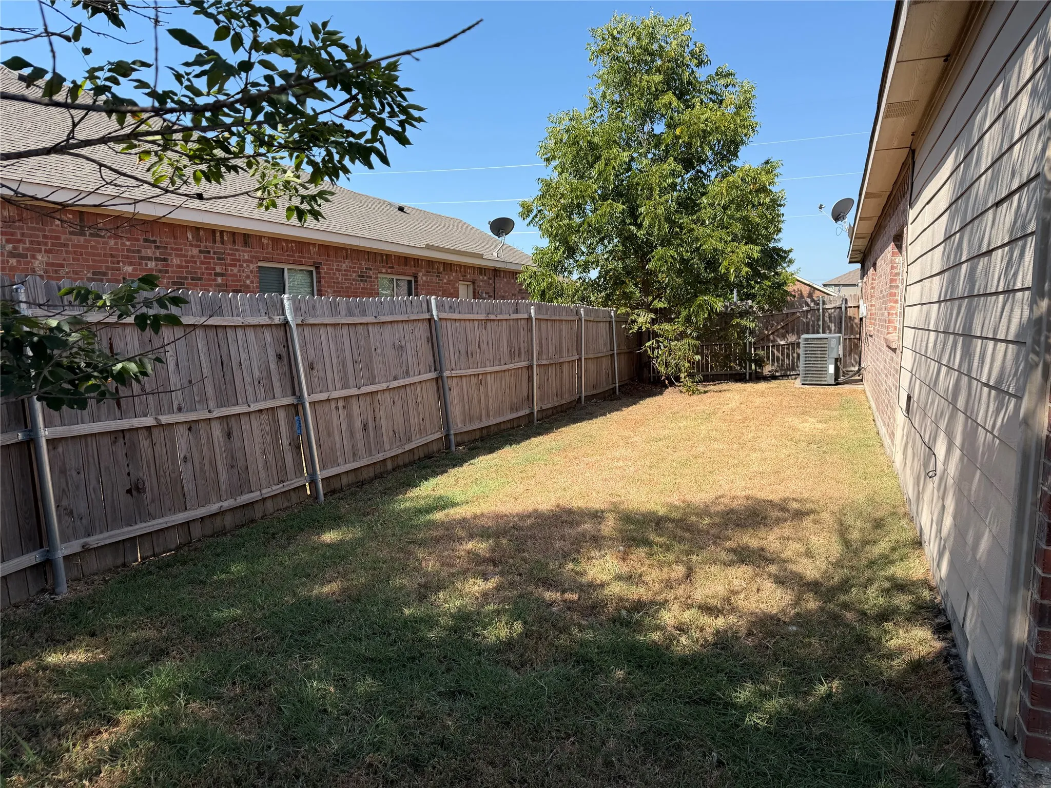 Enclosed backyard featuring a wood fence, mature tree, and a brick and siding exterior