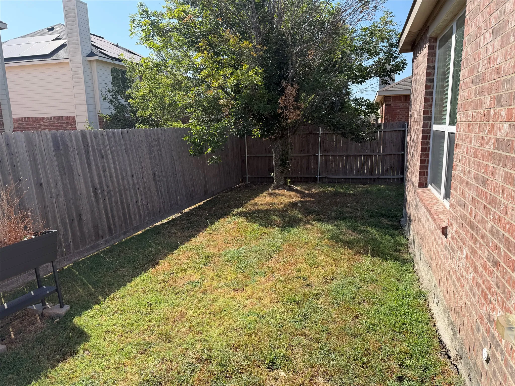 Private backyard with wood fencing, a mature tree, and a brick exterior wall featuring a window