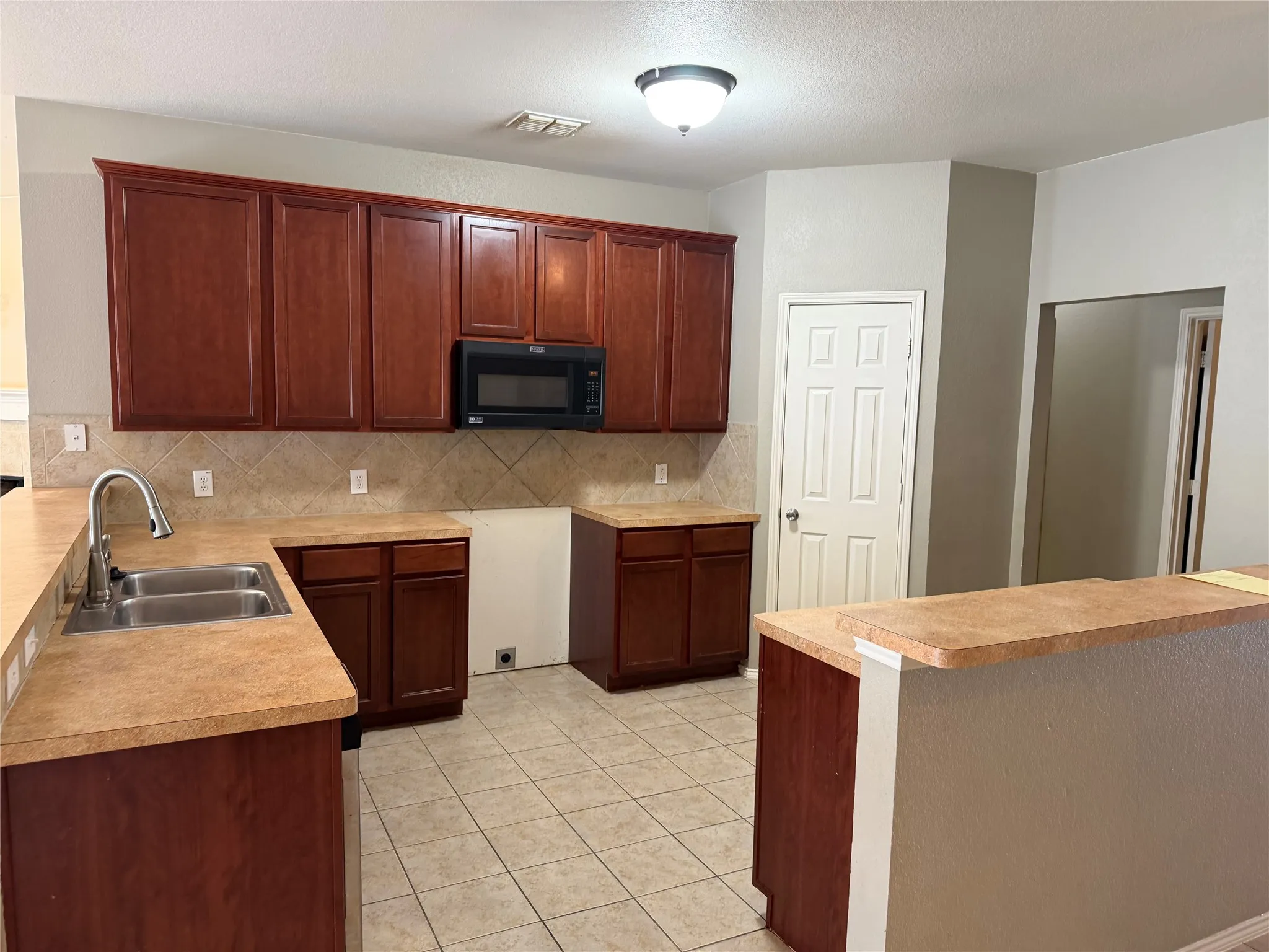 Kitchen featuring wood-finish cabinetry, tile flooring, a stainless steel double sink, a built-in microwave, and an integrated breakfast bar