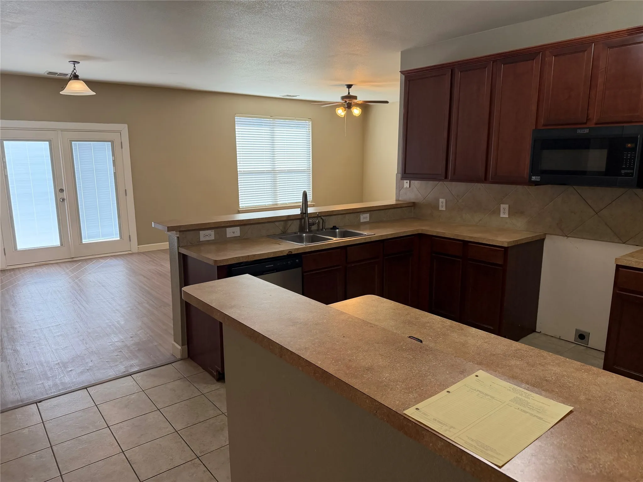 U-shaped kitchen with laminate countertops, wood-finish cabinetry, tile backsplash, and stainless steel sink
