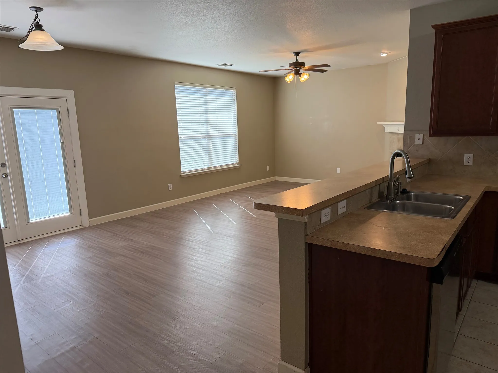 Wood-finish flooring throughout, ceiling fan with integrated lighting, kitchen featuring a double basin stainless steel sink, and a breakfast bar