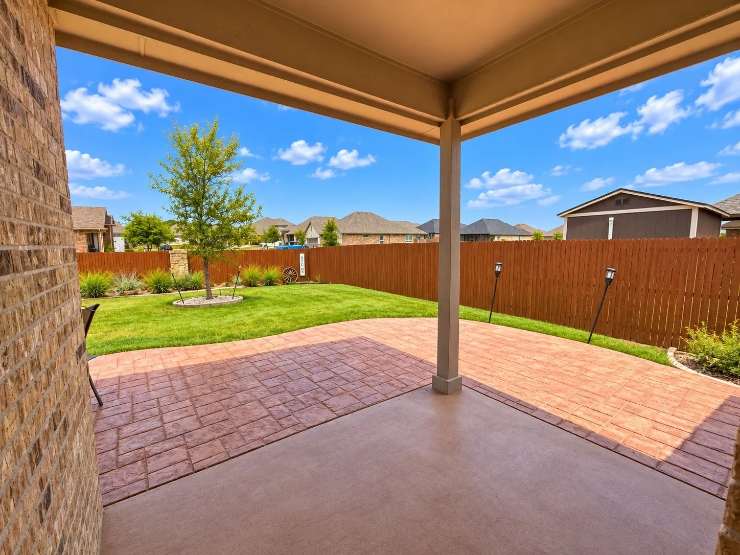 Covered patio with stamped concrete flooring, brick exterior, and a privacy fence