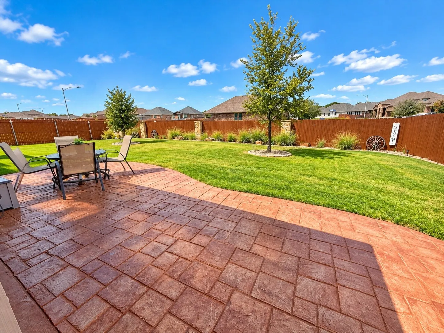 Expansive backyard featuring a stamped concrete patio, manicured lawn, and privacy fencing