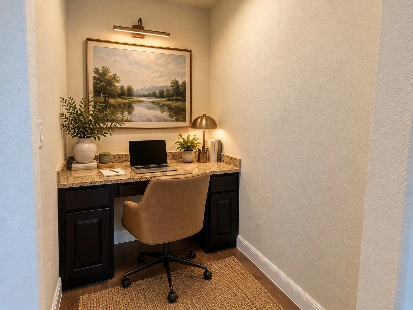 Dedicated home office nook featuring a black cabinetry desk with stone-finish countertop, brass dome pendant lighting, natural fiber area rug, and framed landscape artwork