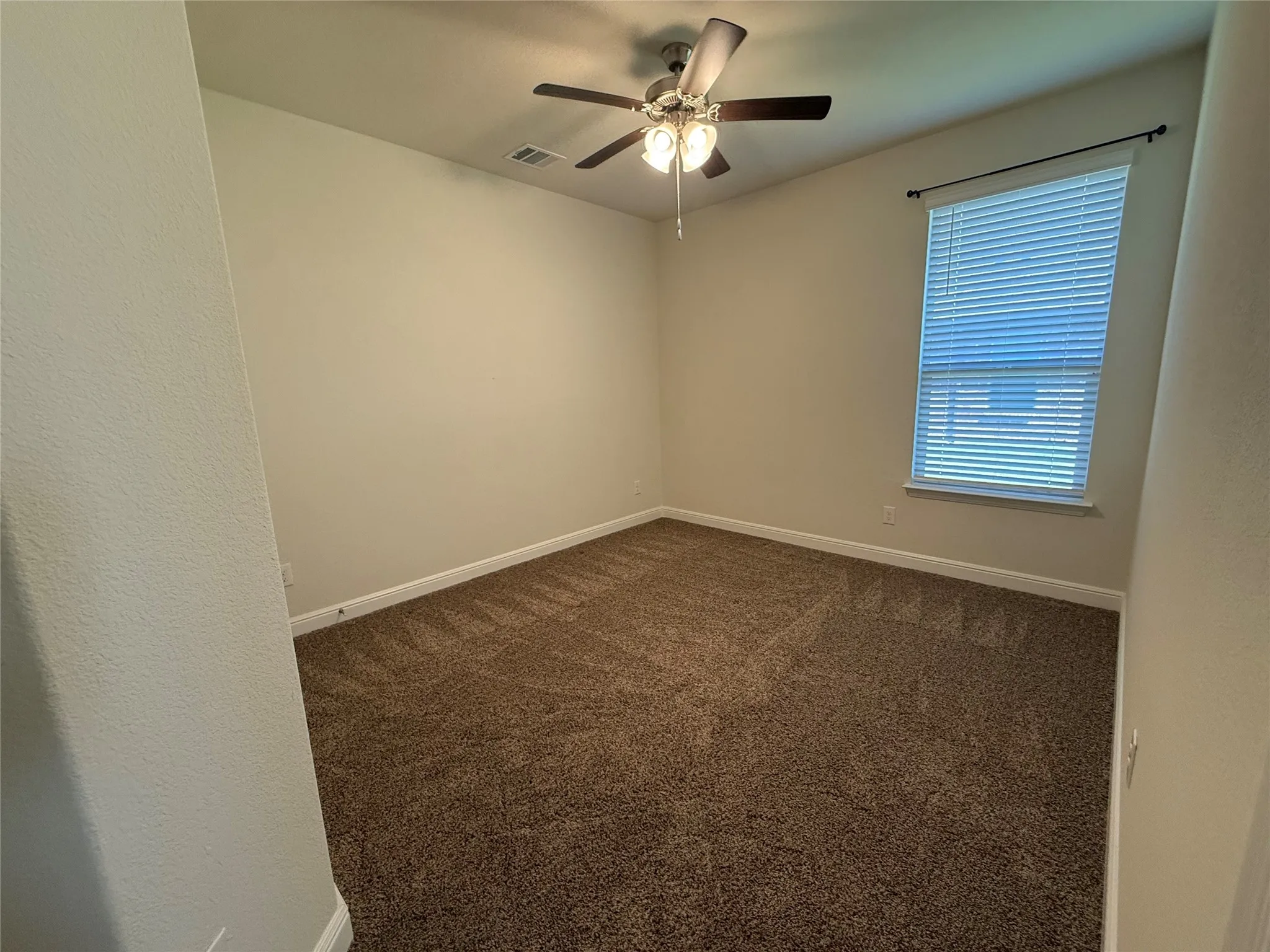 Bright corner bedroom with neutral wall finishes, carpeted flooring, and a ceiling fan with integrated lighting