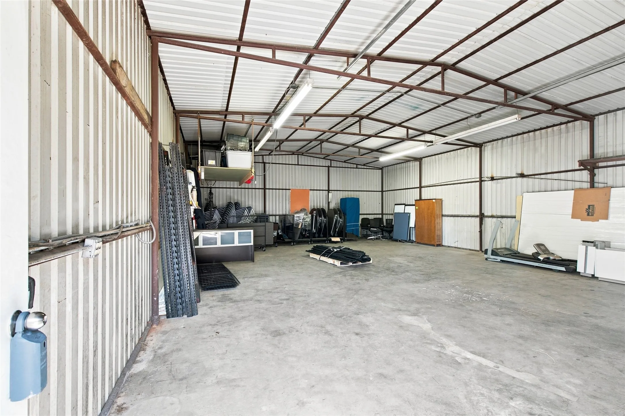 Spacious interior featuring a concrete floor, corrugated metal walls, exposed metal framing, and overhead fluorescent lighting