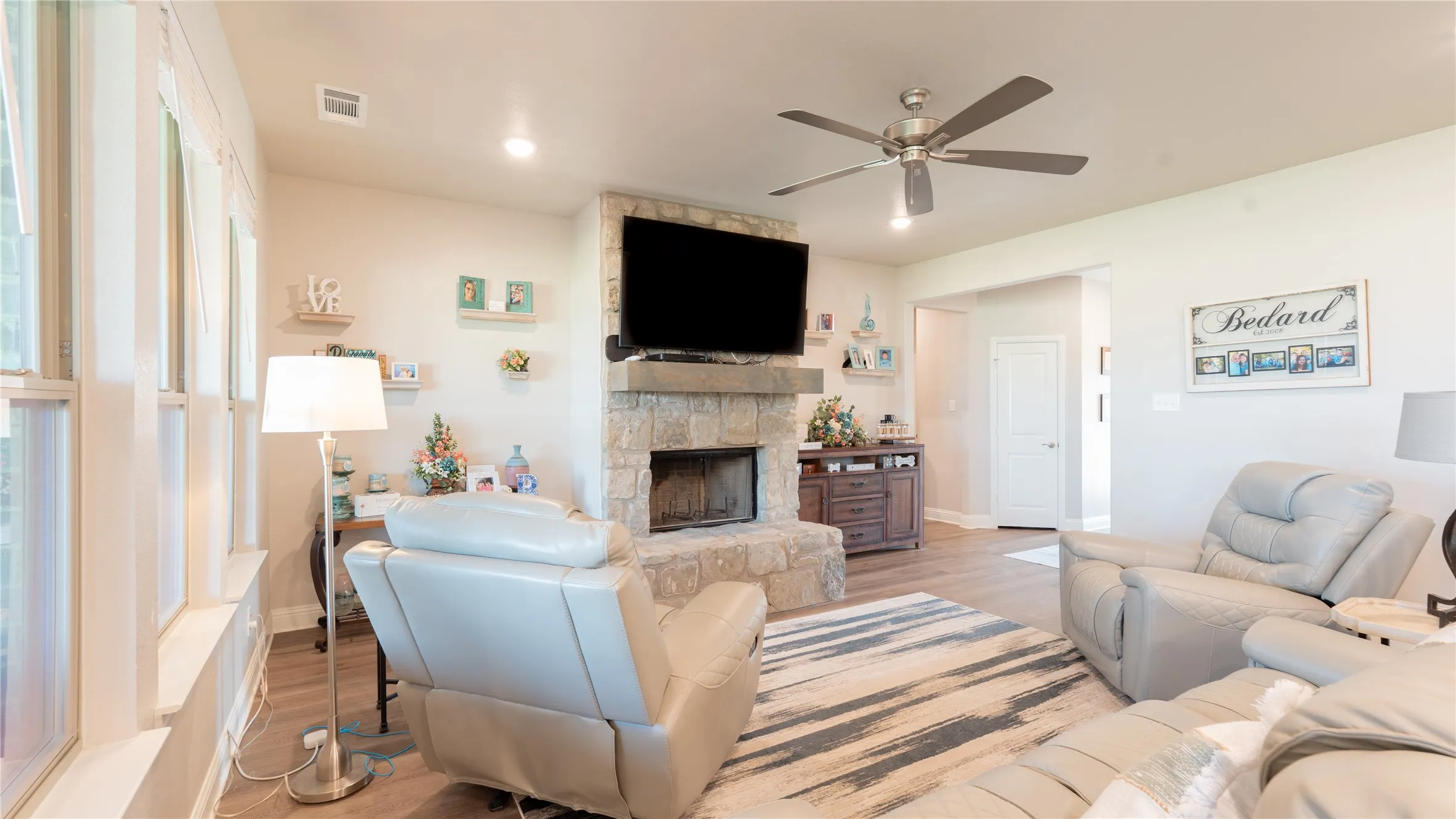 Stone fireplace with a large mantel, wood-finish flooring, recessed lighting, and a ceiling fan