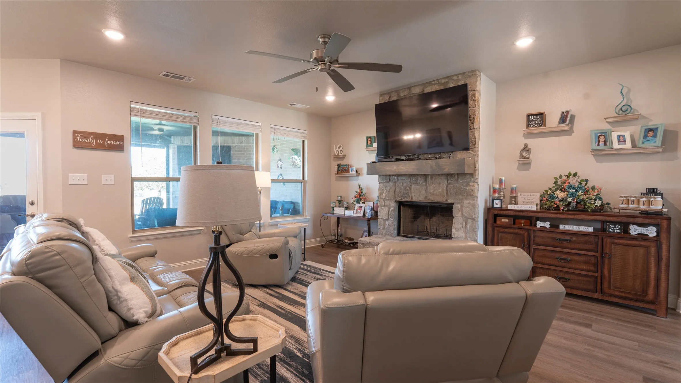 Recessed lighting, ceiling fan, stone-clad fireplace with mantel, multiple windows, and wood-finish flooring