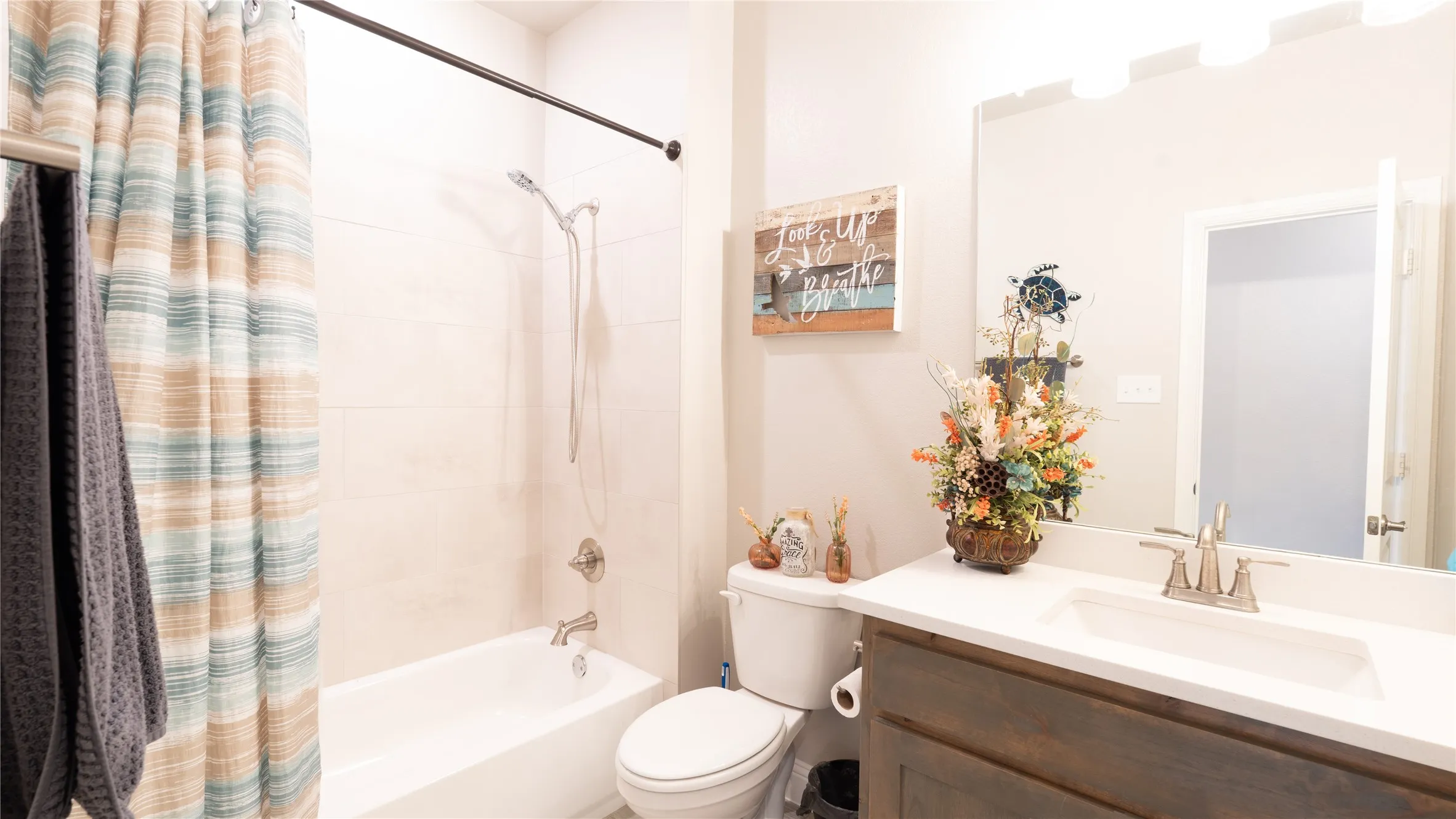Bathroom featuring a built-in tub with shower, tiled shower surround, single-basin vanity with a light-colored countertop, and a vanity mirror with overhead lighting