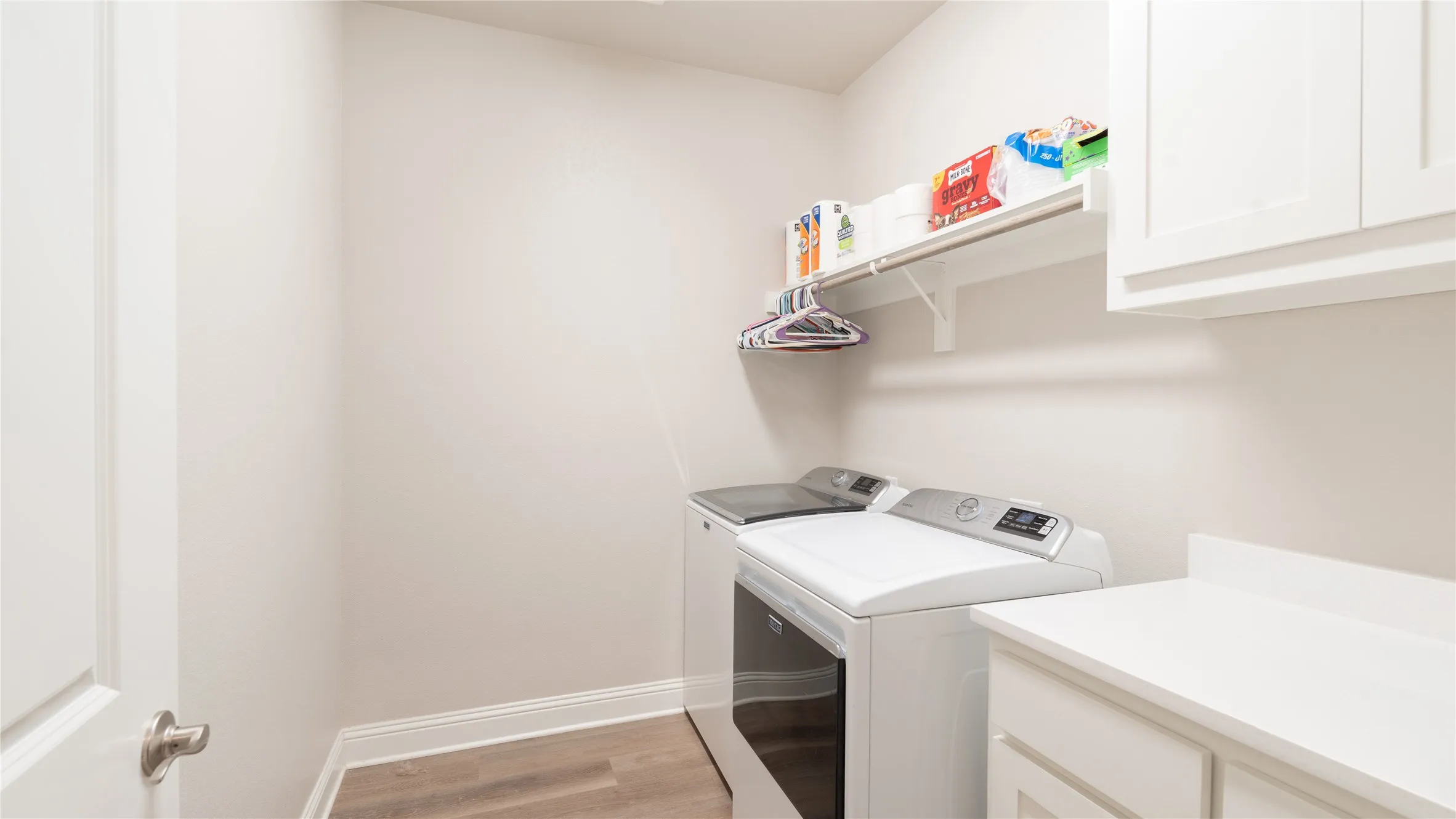 Laundry space featuring wood-finish flooring, white cabinetry, a built-in shelf, and a clothing rod