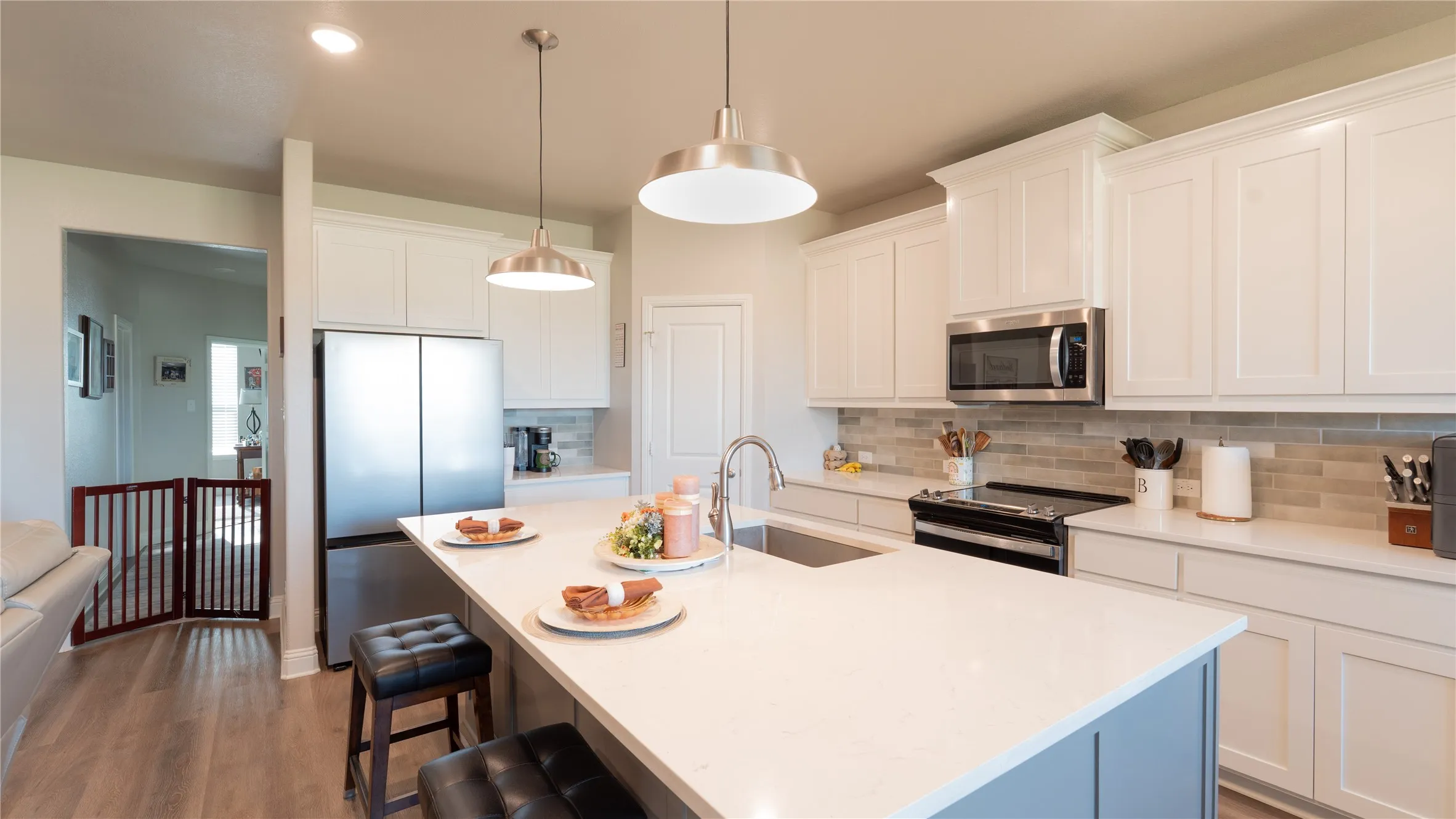White cabinetry with crown molding, stainless steel appliances, light-toned backsplash, quartz countertops, and pendant lighting