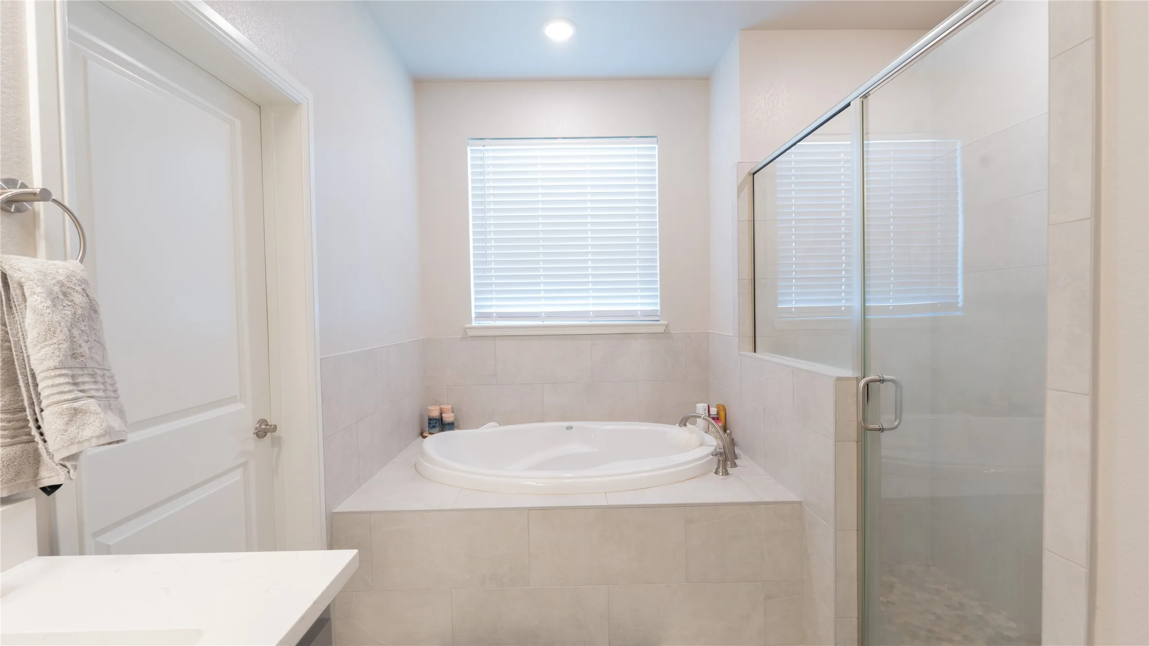 Built-in soaking tub with a tiled surround, glass-enclosed shower, and a privacy window with blinds