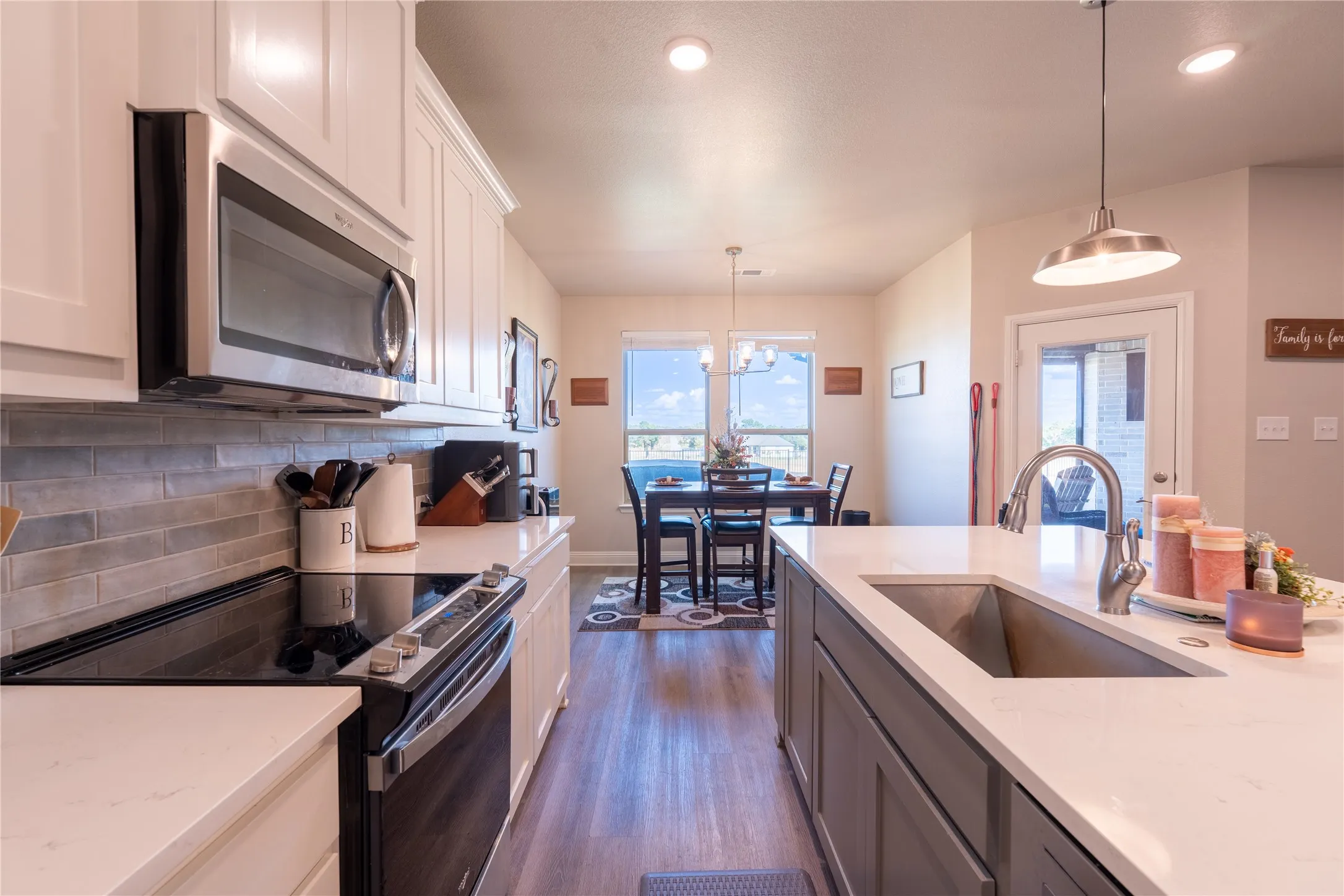 Kitchen featuring a central island with an undermount sink, stainless steel appliances, wood-finish flooring, and light-toned cabinetry