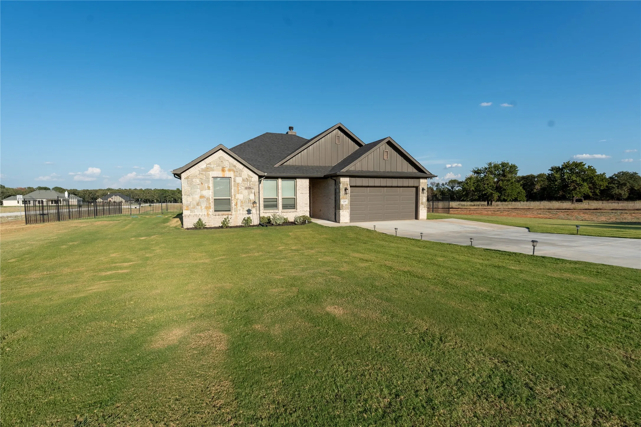 Stone and siding exterior with a dark shingle roof, attached two-car garage, concrete driveway, and front yard landscaping
