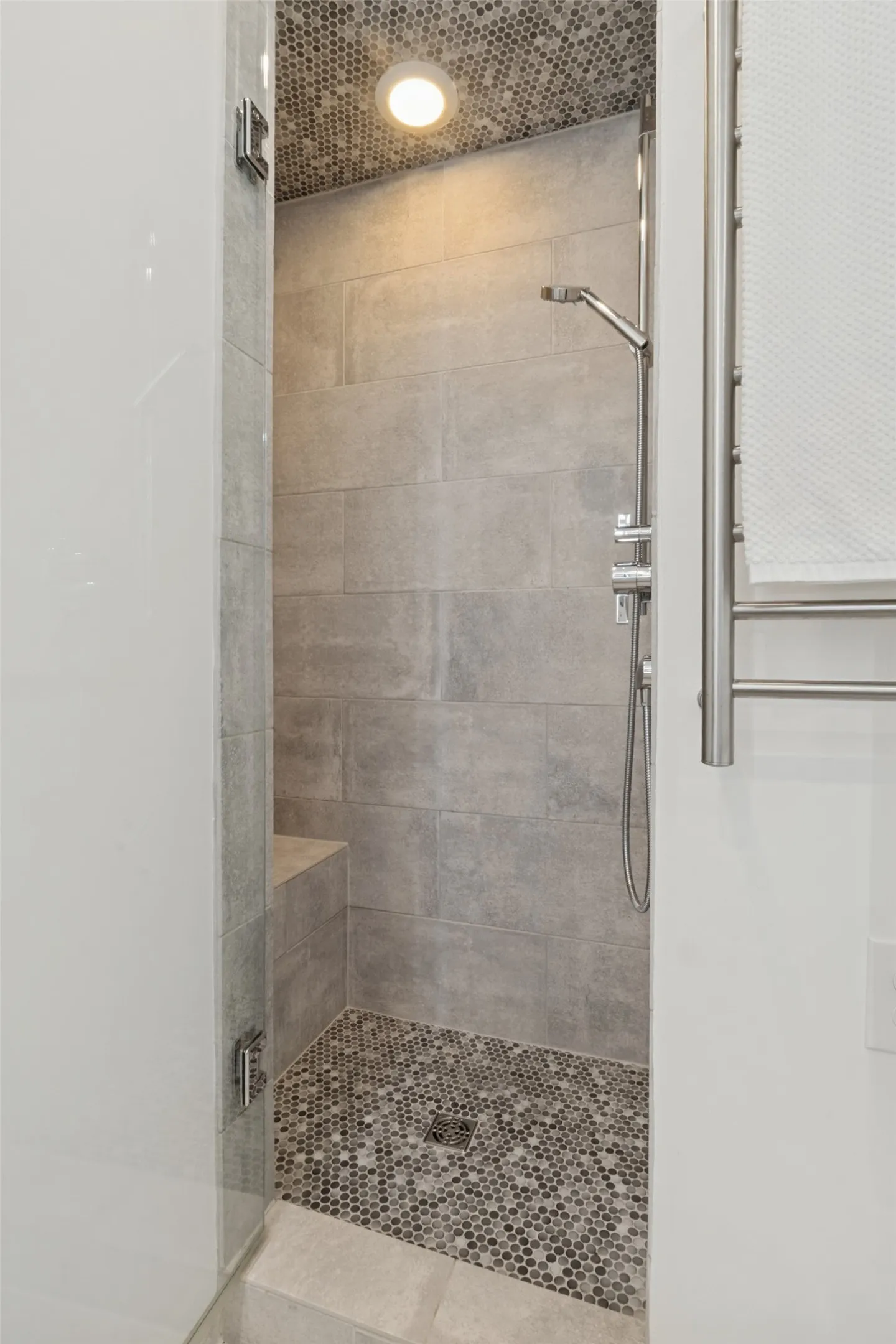 Walk-in shower with tile surround, mosaic tile floor, built-in bench, and glass enclosure