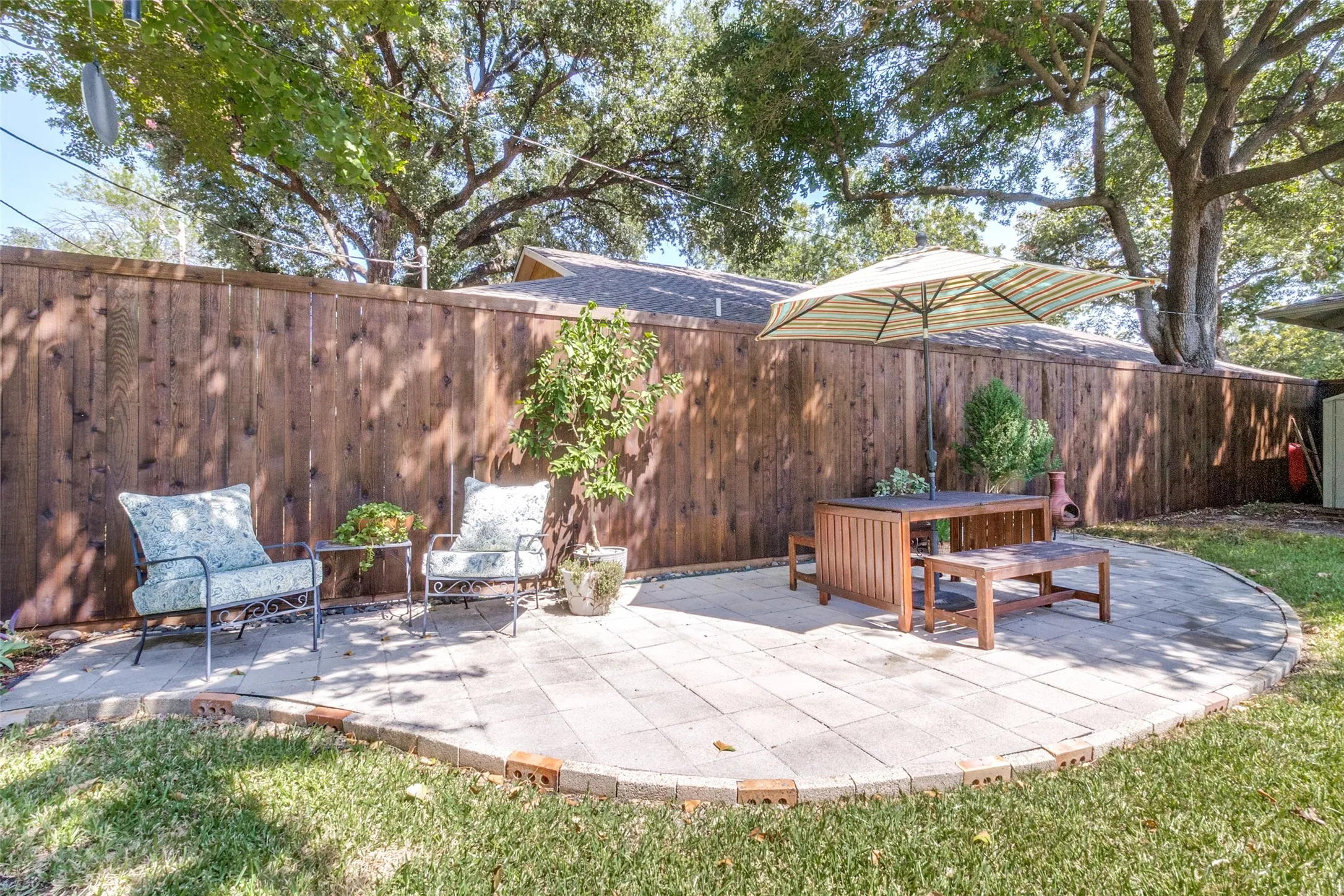 Paved stone patio area with a brick border, surrounded by a wood privacy fence