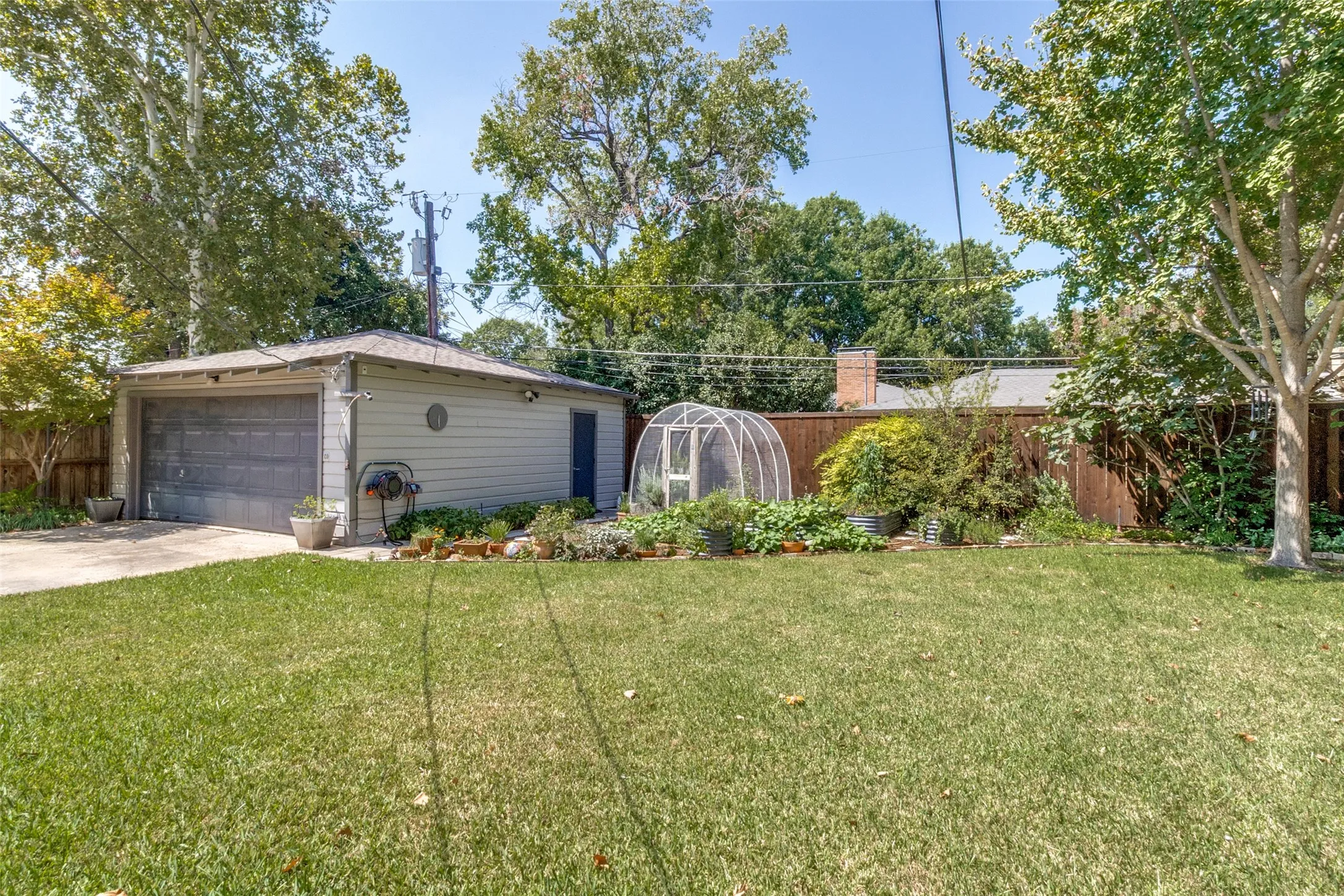 Expansive grassy yard with a detached garage, a small greenhouse structure, and a wood-paneled fence