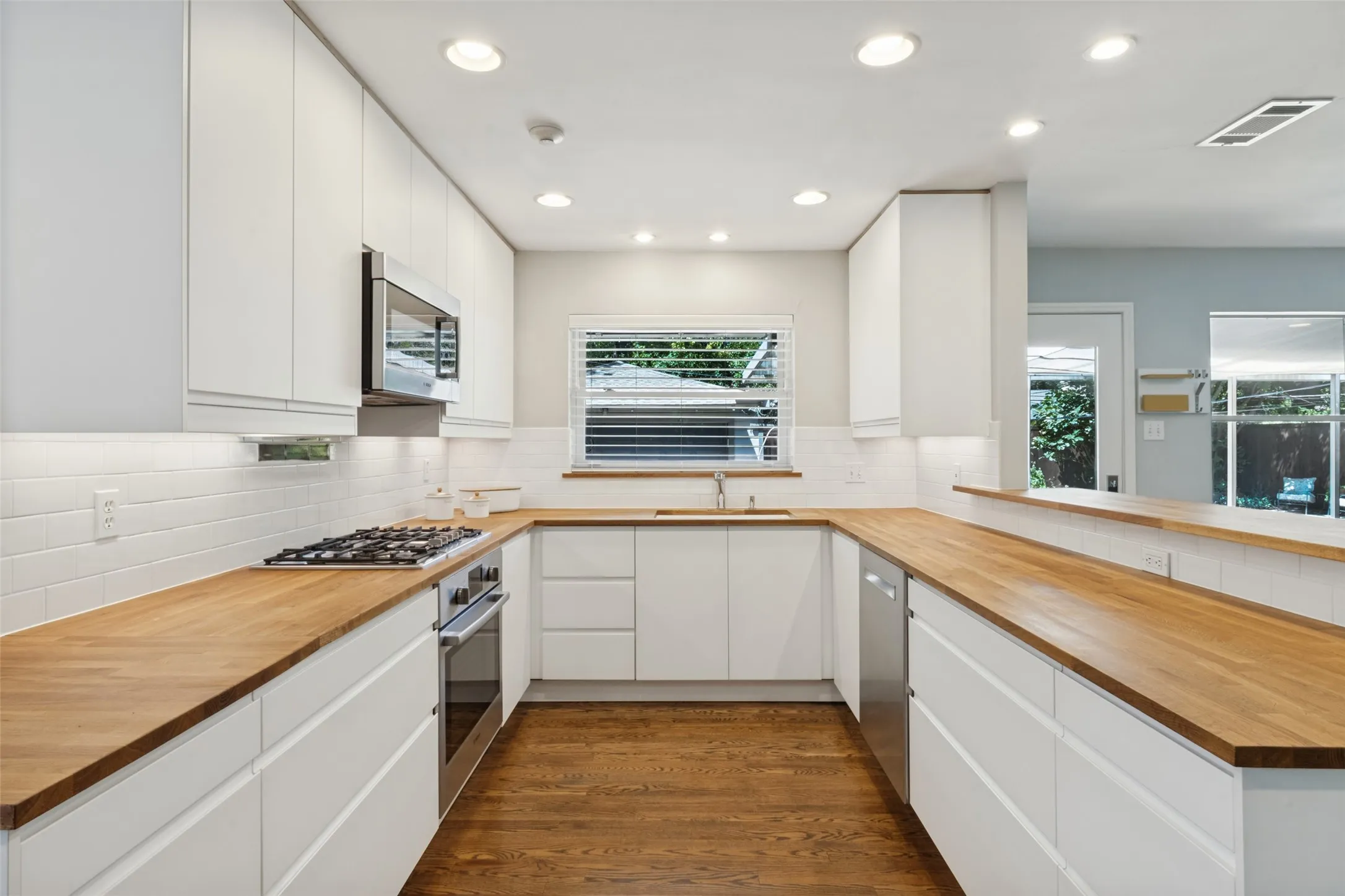 Kitchen featuring wood-finish countertops, white flat-panel cabinetry, stainless steel appliances, a subway tile backsplash, and recessed lighting