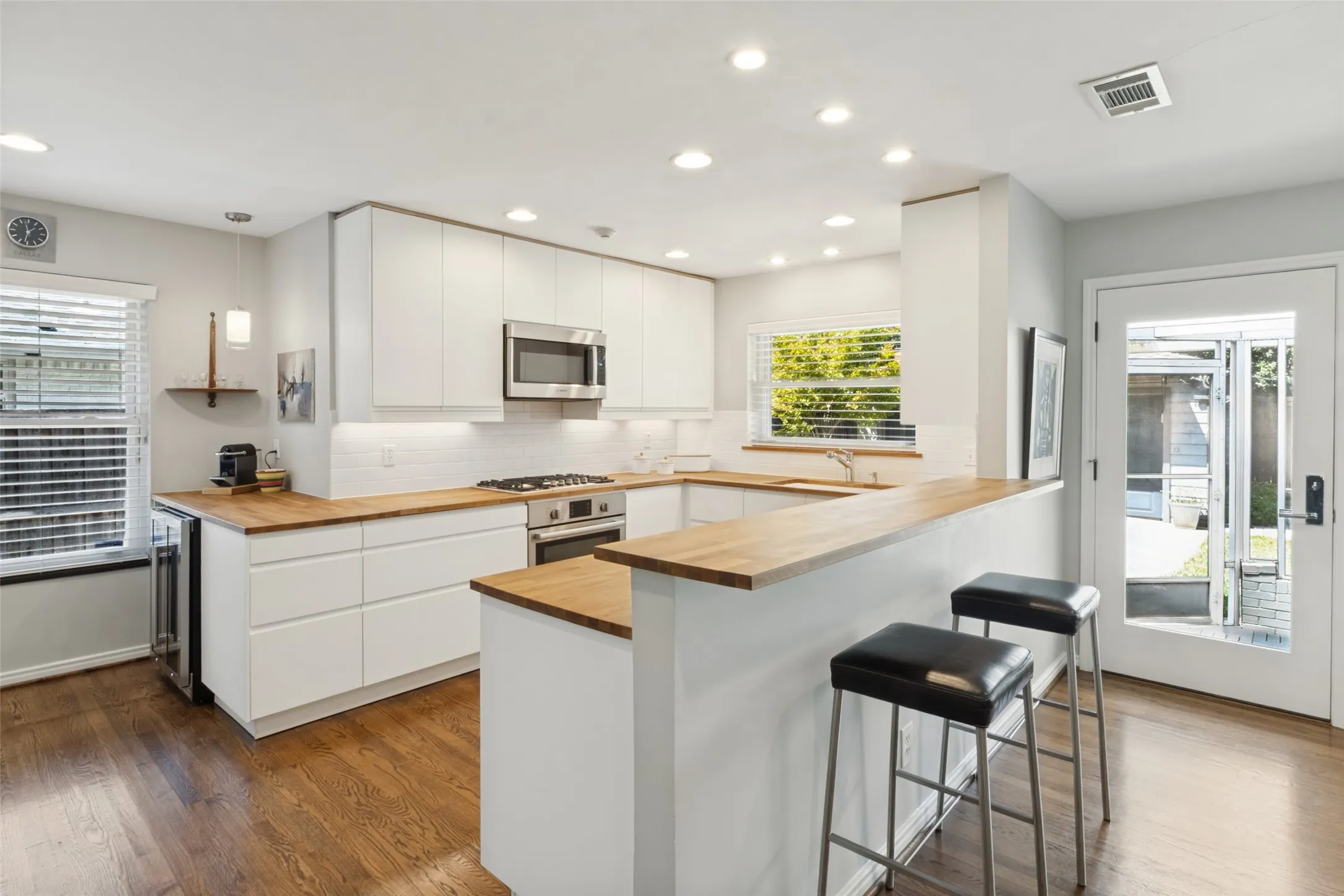 U-shaped kitchen featuring wood-finish countertops, white flat-panel cabinetry, stainless steel appliances, a subway tile backsplash, and recessed lighting