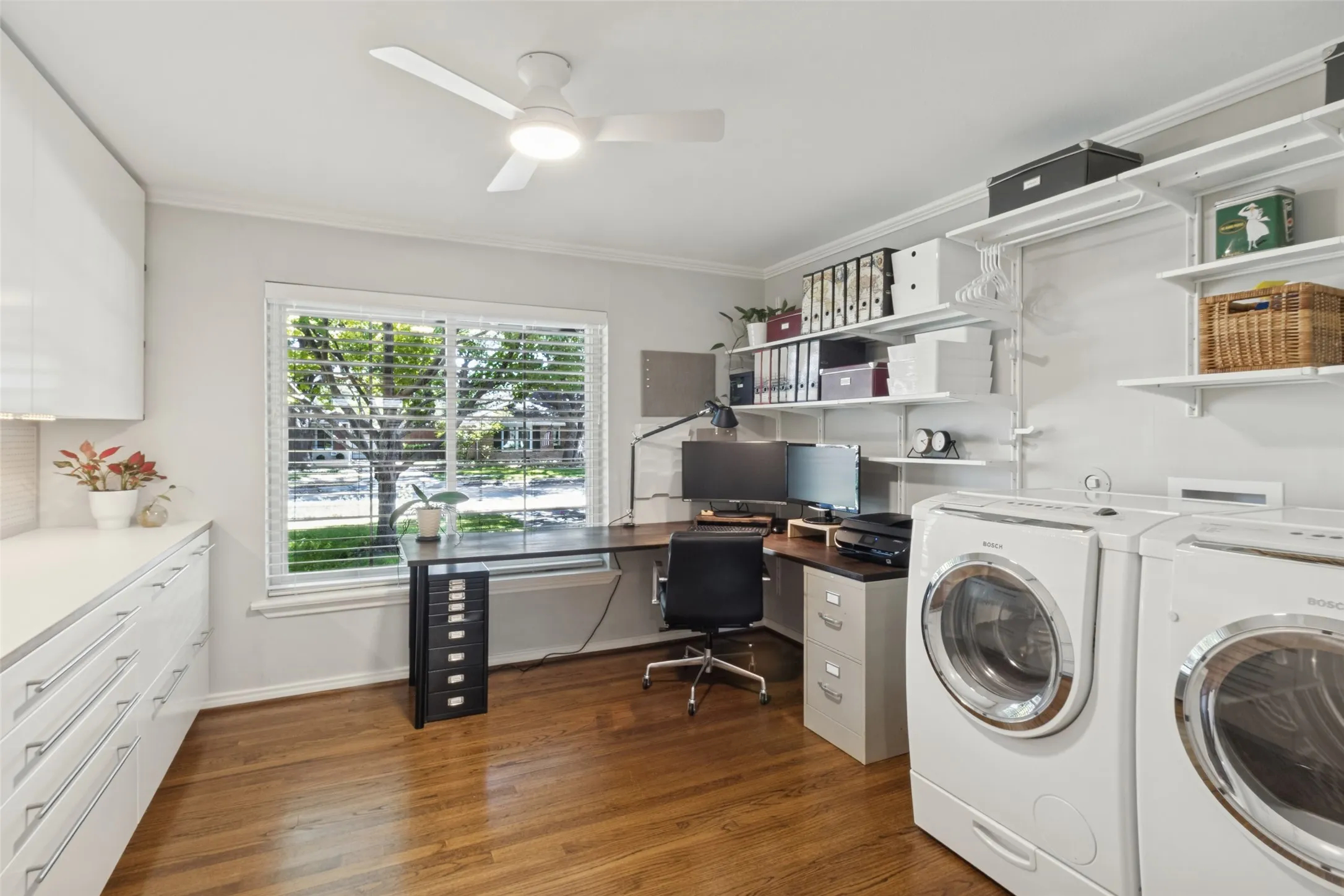 Wood-finish flooring, built-in shelving, white cabinetry with integrated hardware, and a window with horizontal blinds