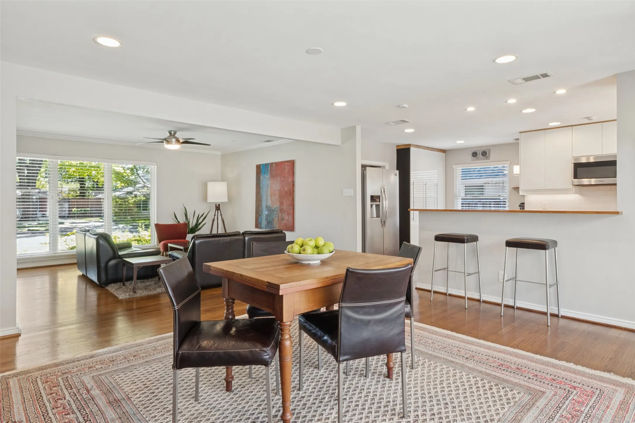 Wood-finish flooring throughout, recessed lighting, white kitchen cabinetry, stainless steel appliances, and a kitchen peninsula with bar seating