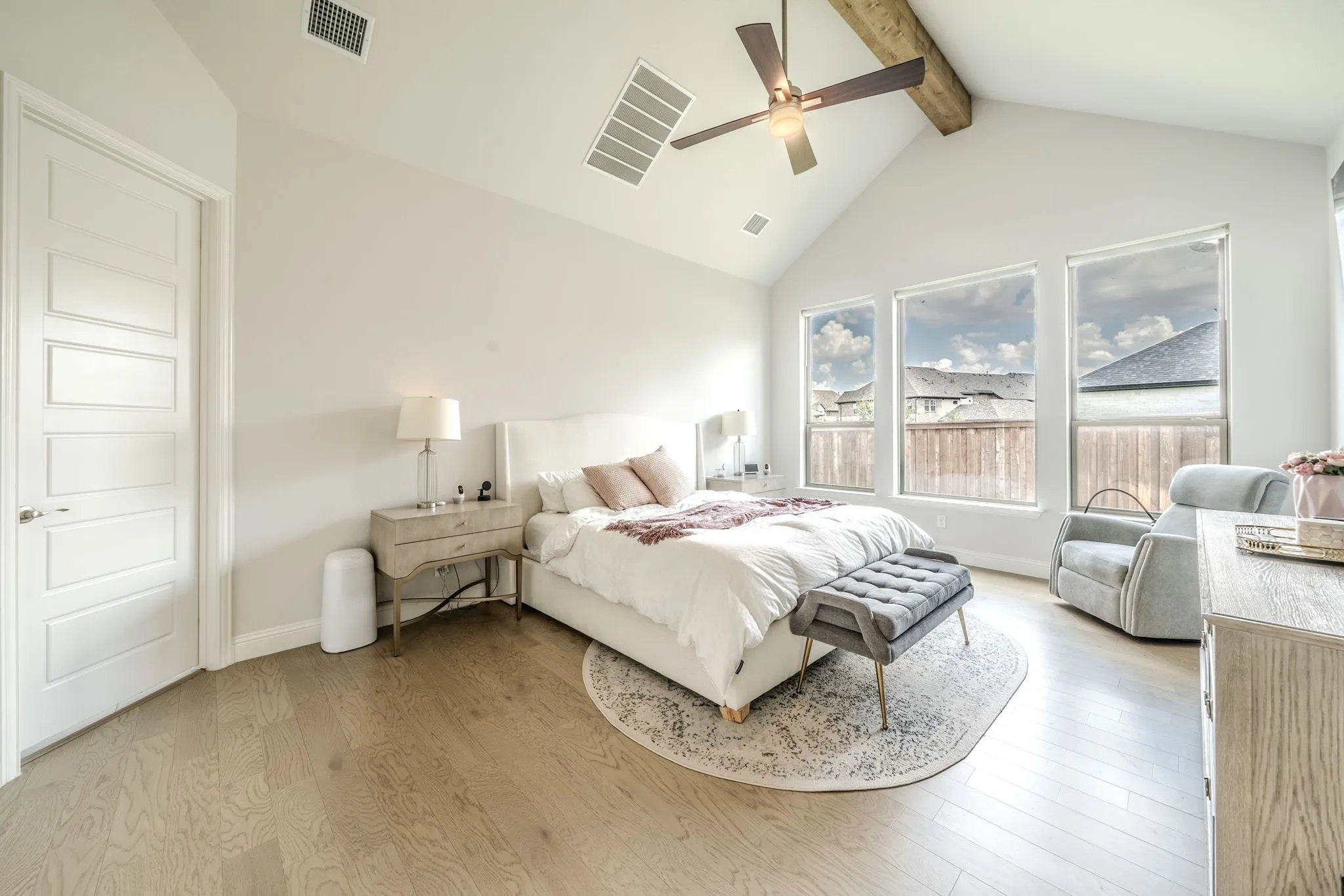 Vaulted ceiling with exposed wood beam, ceiling fan, wood-finish flooring, and multiple windows