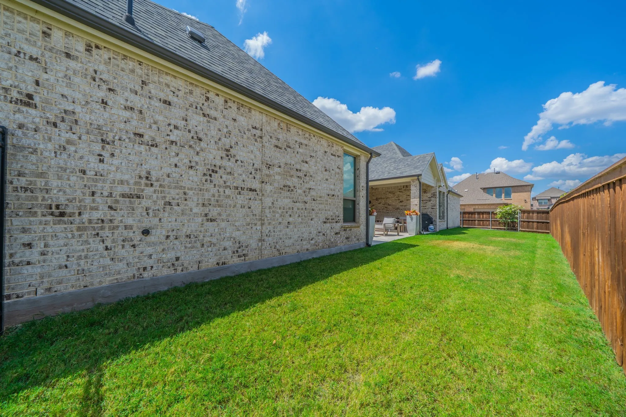 Expansive grassy yard with a wooden privacy fence, brick exterior, and covered patio