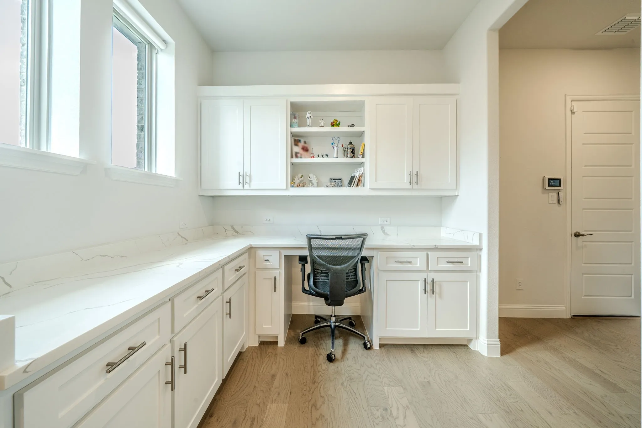 Built-in desk with white cabinetry, open shelving, and light-colored countertops