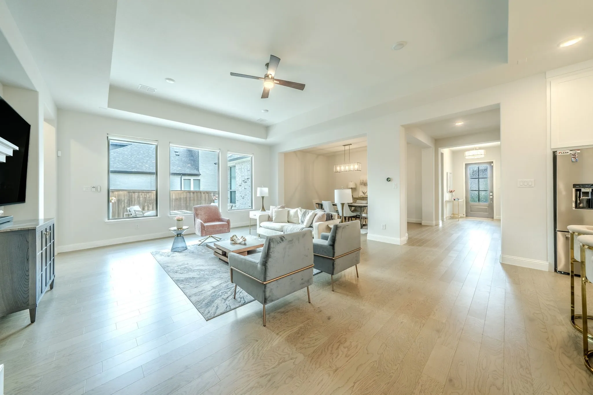 Tray ceiling with a ceiling fan, three large windows, wood-finish flooring, recessed lighting, and a stainless steel refrigerator