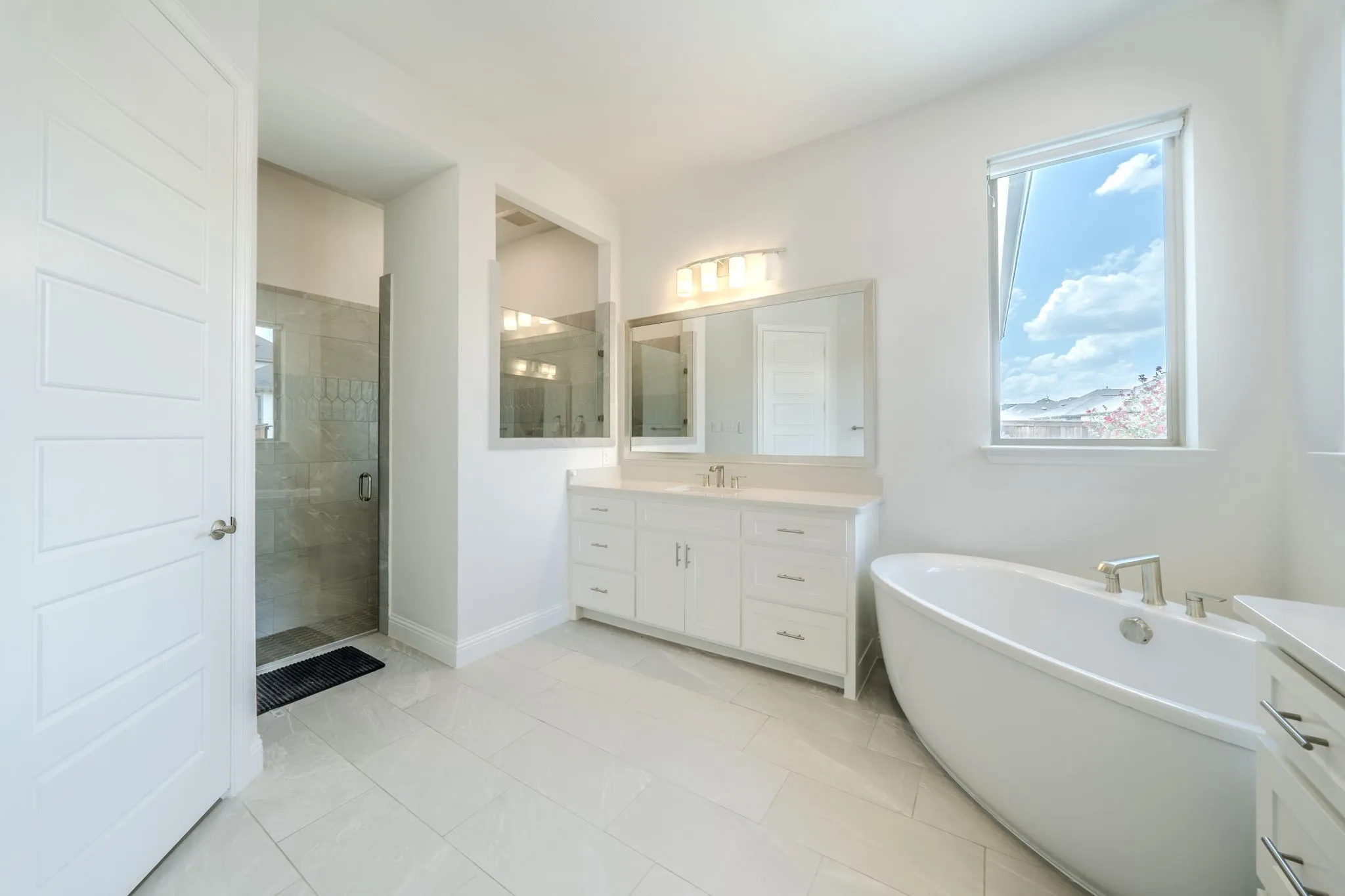Freestanding soaking tub, dual vanity with quartz countertop, tiled walk-in shower with glass enclosure, and large window with mountain scenery