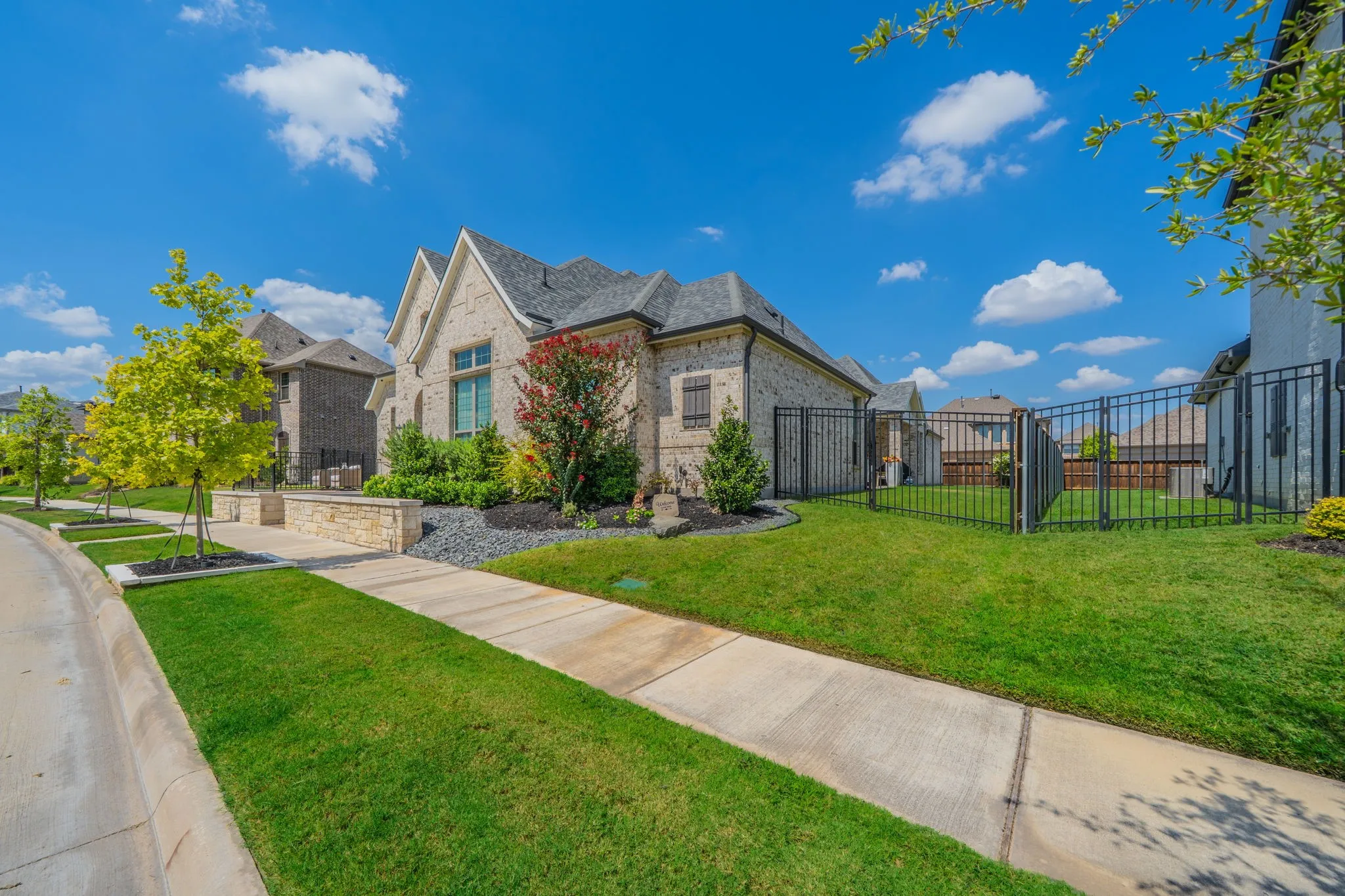 Stone facade exterior with gabled roofline, mature landscaping, sidewalk access, and wrought iron fencing