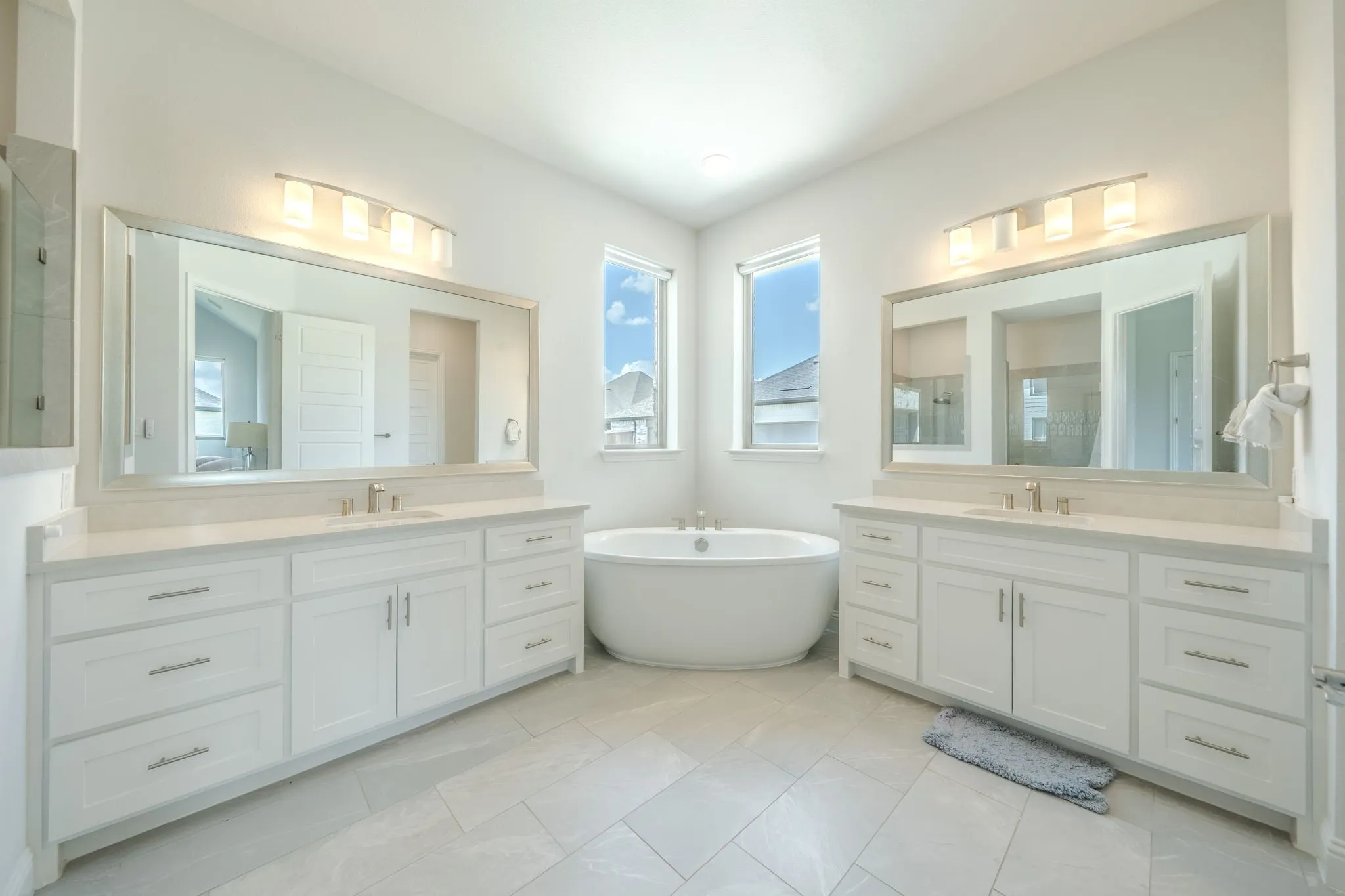 Freestanding soaking tub, dual vanity with undermount sinks, stone countertops, framed mirrors, and tile flooring